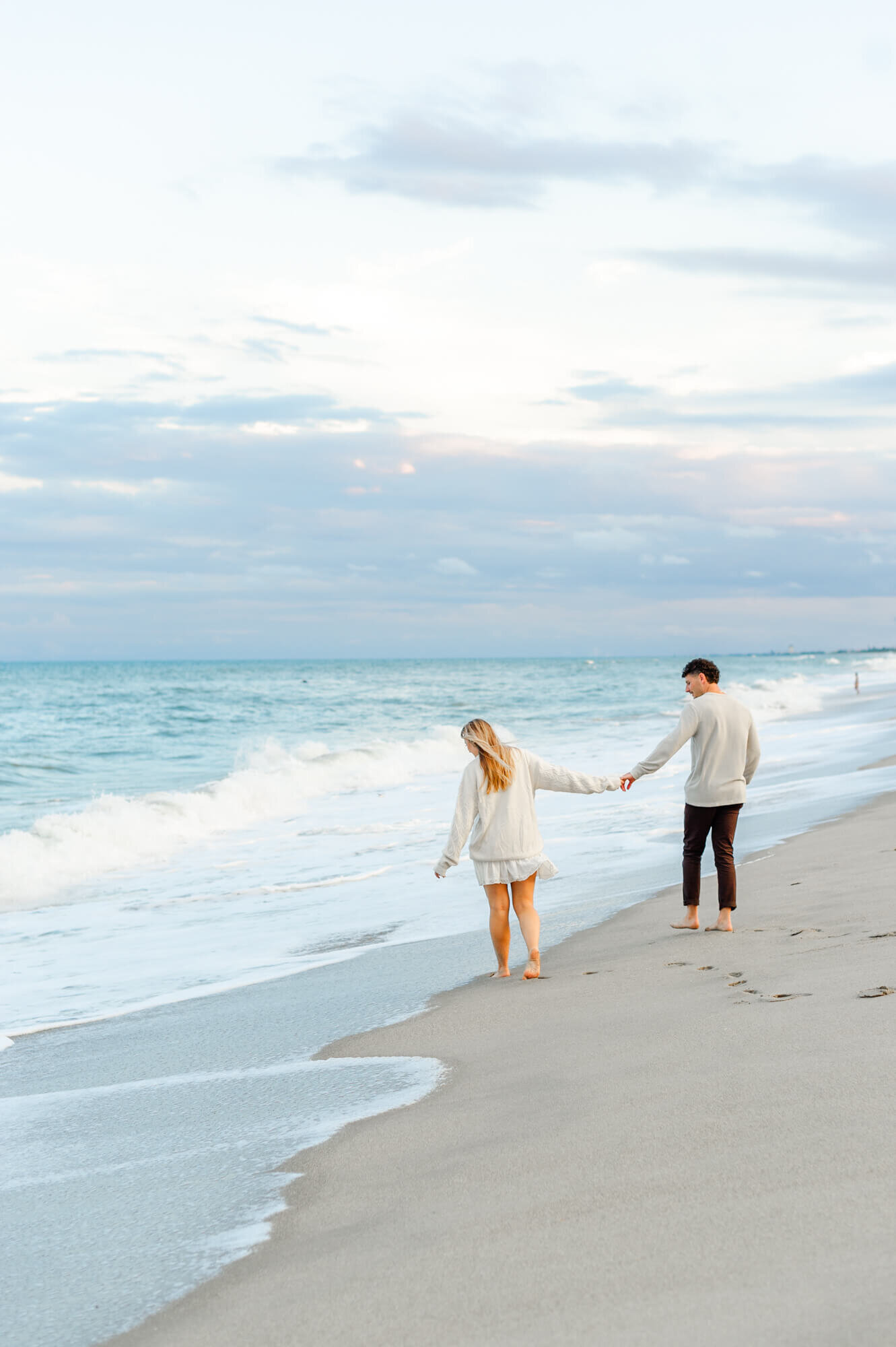 Newly engaged couple walks on the beach as their  Orlando engagement photography snaps photos