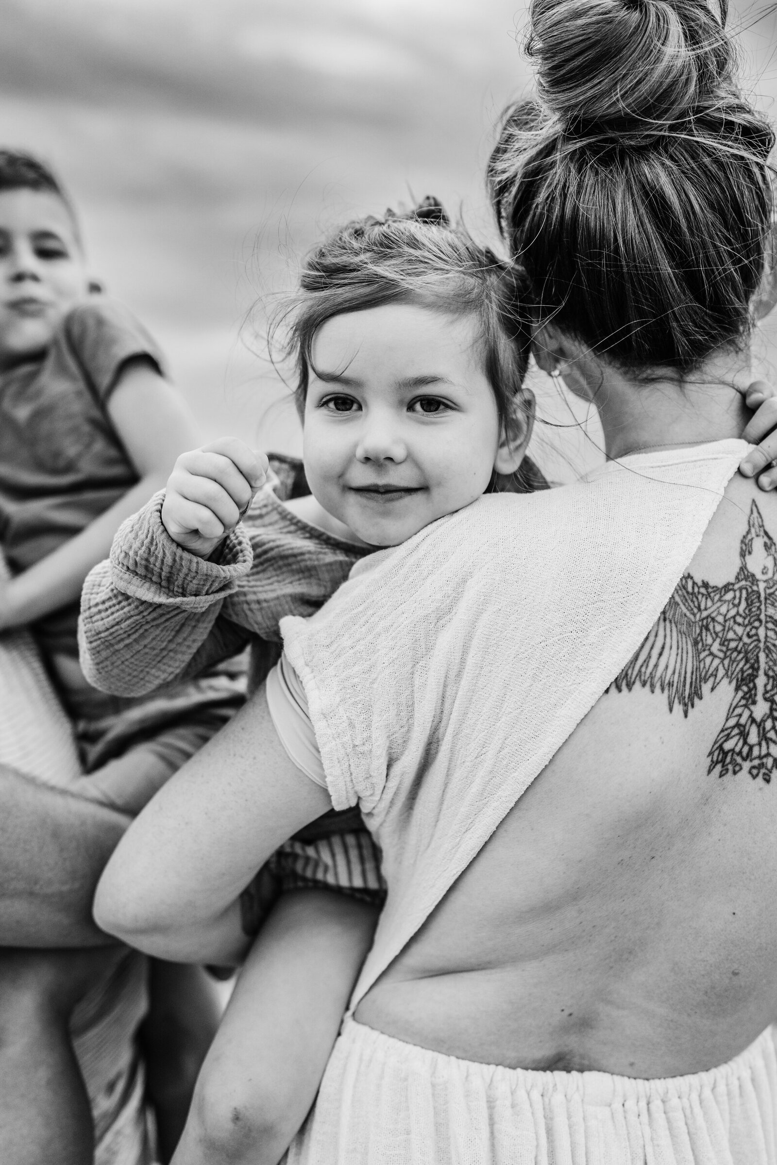toddler girl peeks over moms tattooed back