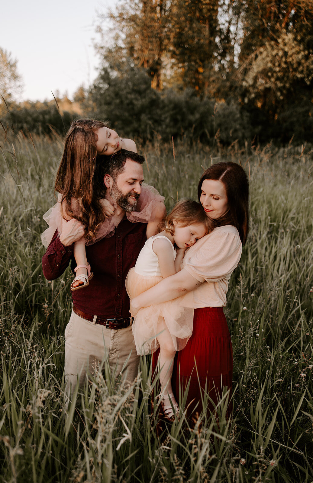 parents snuggling daughters in field