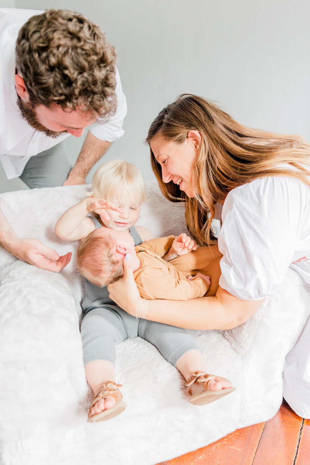 Mom and dad hold newborn in toddler brother's lap