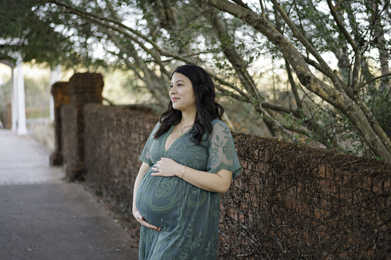 Expecting mother holds her pregnant belly in an emerald green dress during her maternity photos at Athens Botanical Gardens