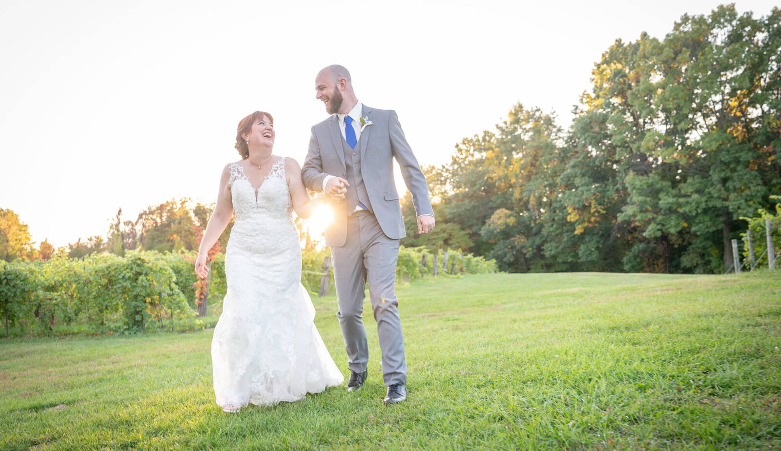 laughing bride and groom walk hand in hand in front of sunset