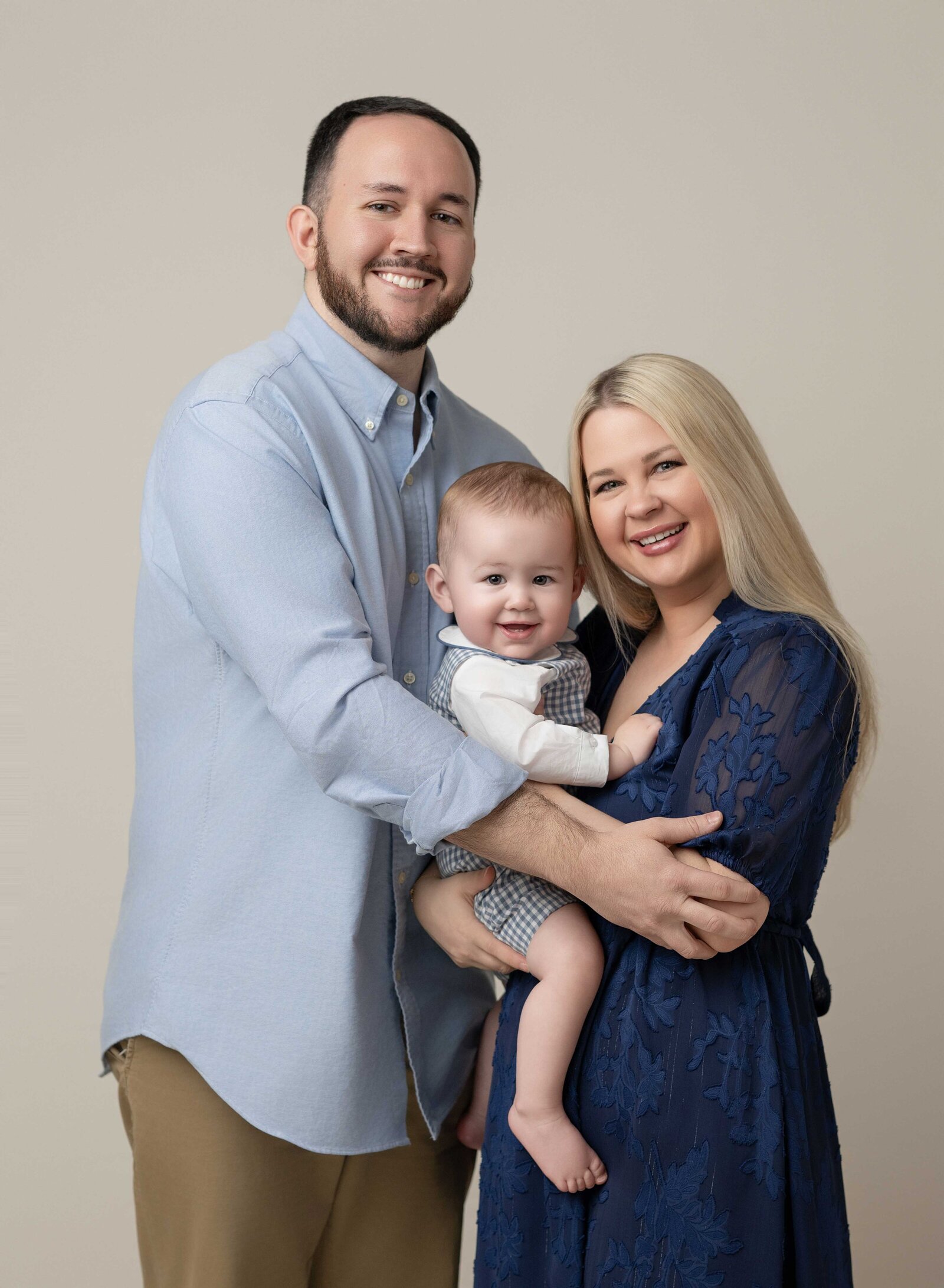 Family dressed in blue outfits and hugging baby boy for a family photo. Family photo taken by Jenni Nikki in Atlanta, GA- 1st birthday photographer.