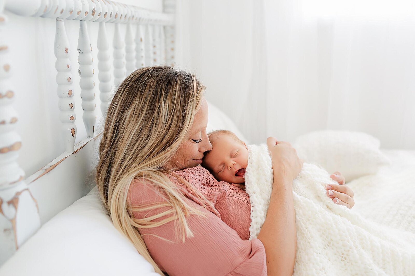 lifestyle photo session of mother holding her newborn while laying in bed