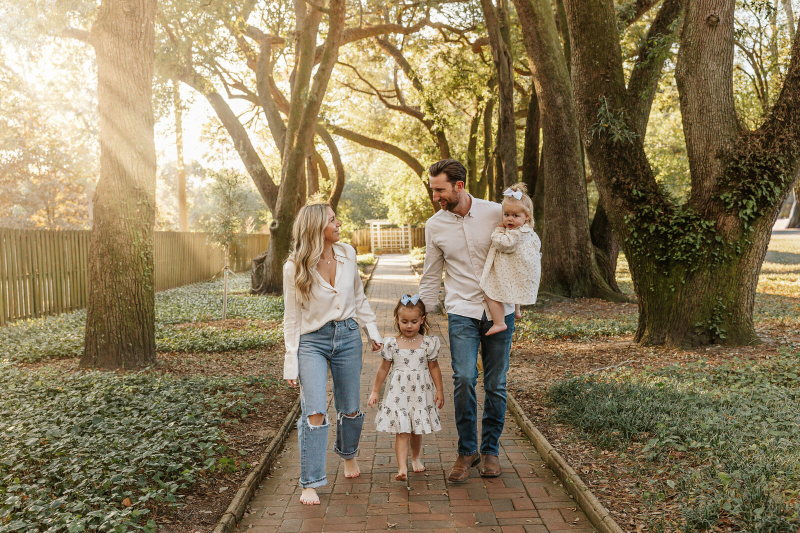 Family session at Hopelands Gardens in Aiken SC - parents walking hand in hand with their two young children under the canopy of oak trees.
