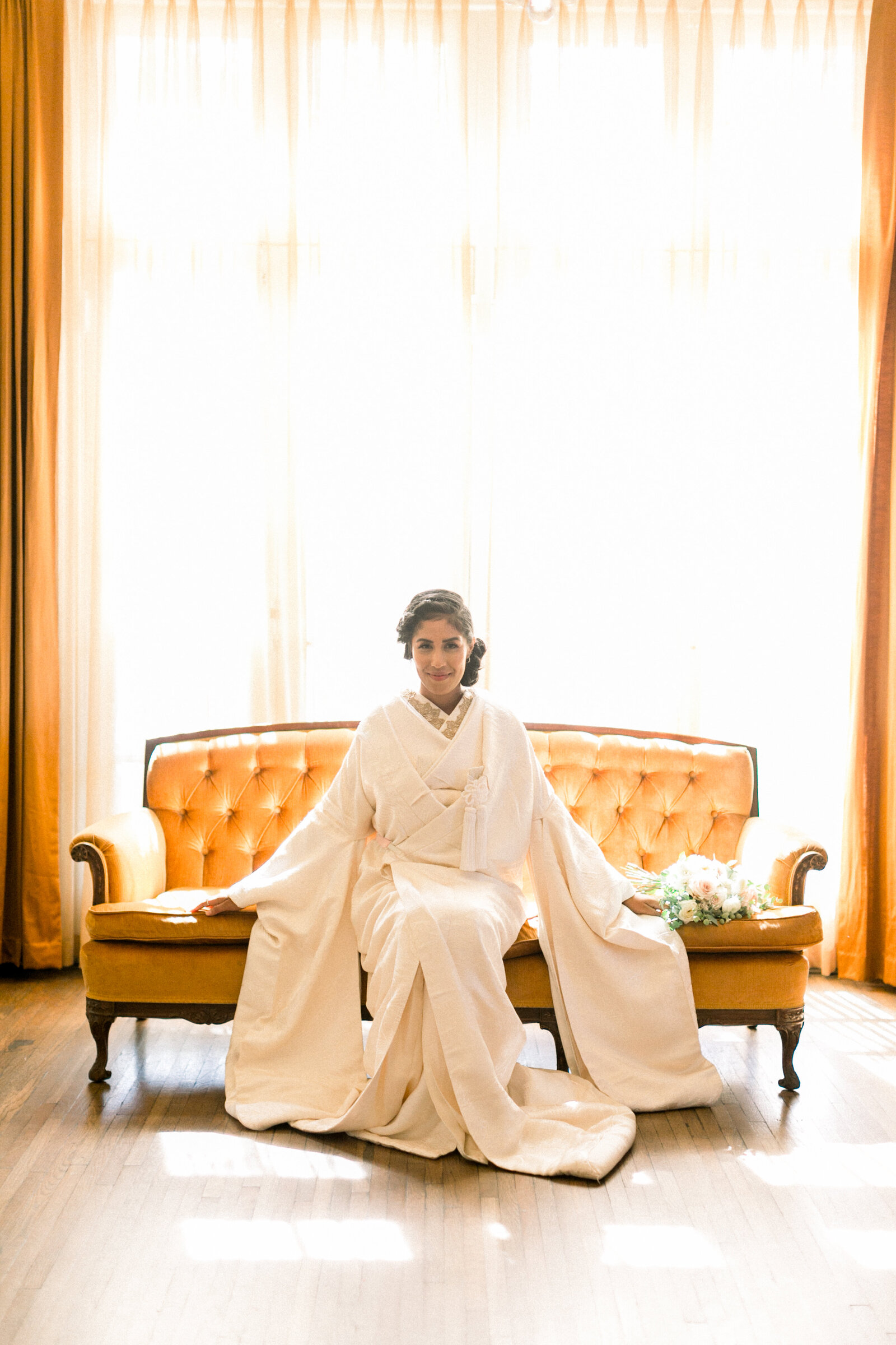 Bride in a traditional white shiromuku wedding kimono seated on a vintage mustard sofa at The Ebell Club Long Beach, Los Angeles California, kimono rental available | ヴィンテージのマスタード色ソファに座る白無垢花嫁 エベルクラブ ロングビーチ ロサンゼルス カリフォルニアで着物レンタル