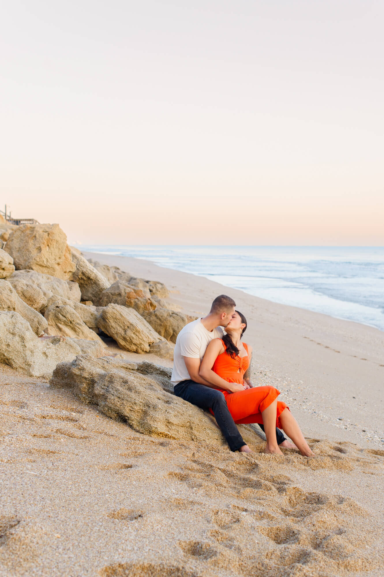 Orlando couple kisses while sitting on rocks at the beach on Cape Canaveral National Seashore