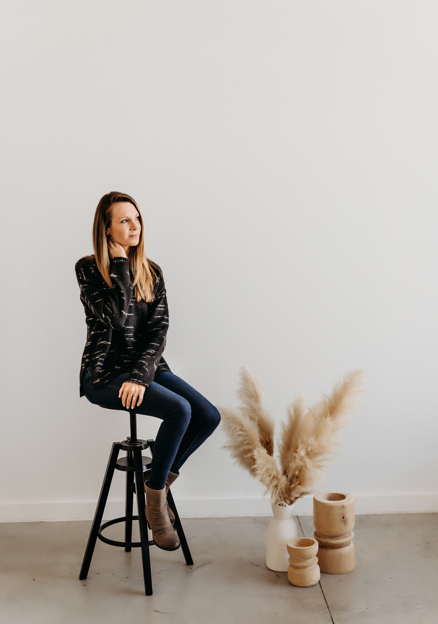 Branding Photographer, a woman sits on a stool in an empty room, only a some pots with pampas grass