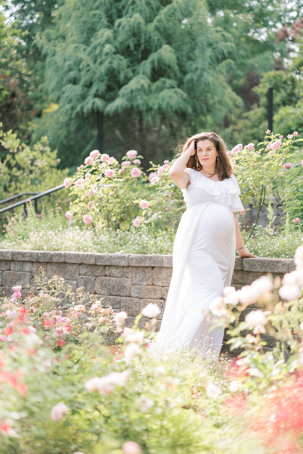 Woman in white dress with baby bump stands in Athens Botanical gardens
