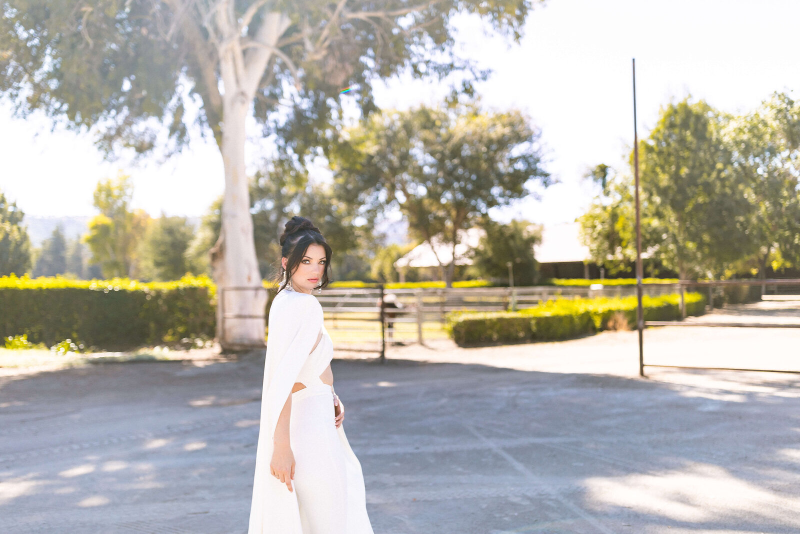 girl with dark hair posing in a green park wearing a white jumper