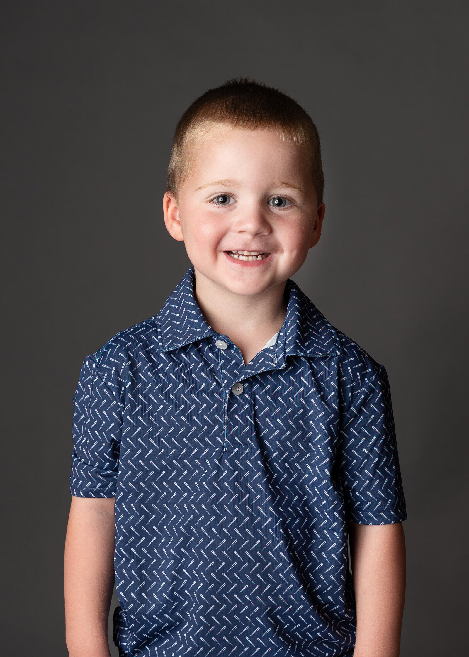 A happy kindergarten boy smiling widely for his school photo.
