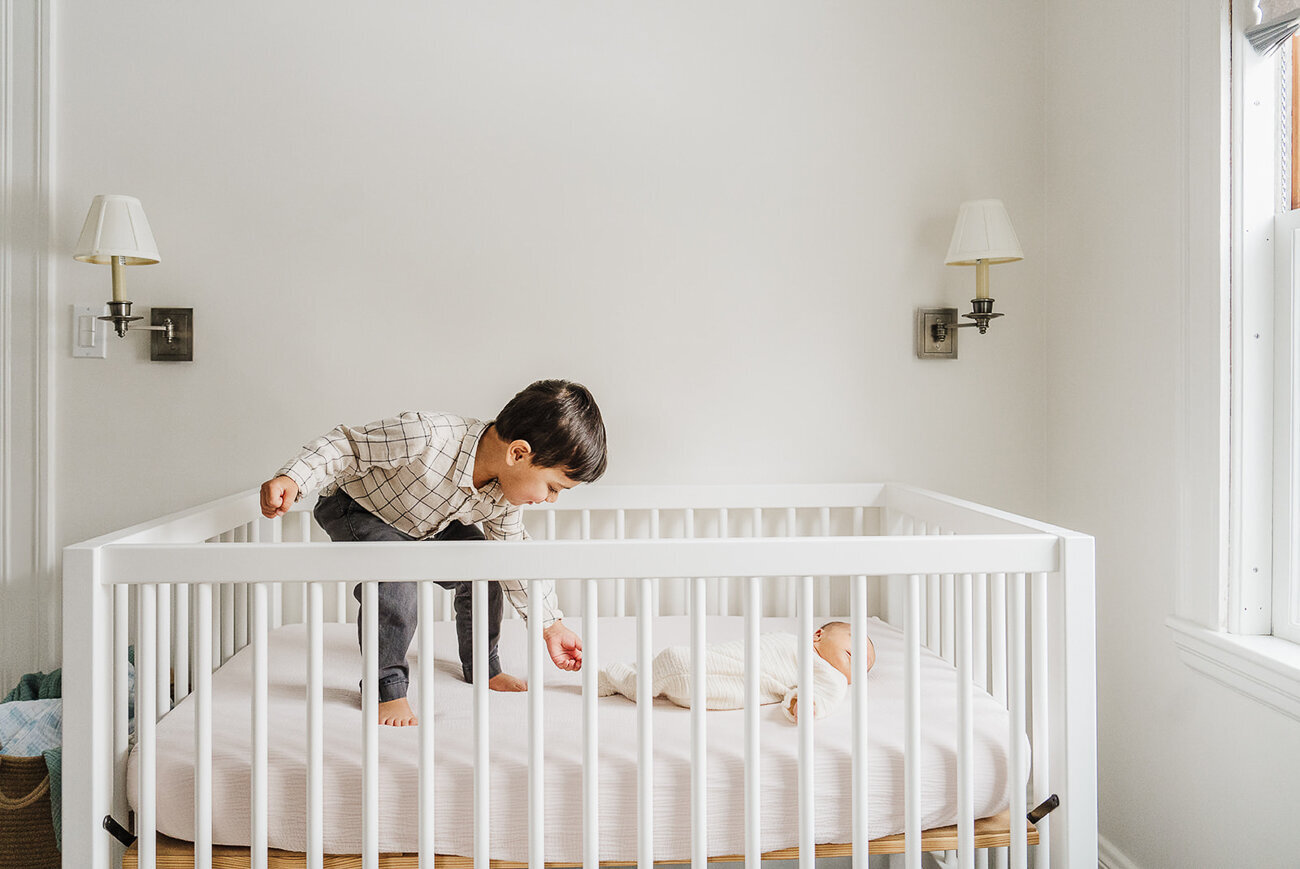 big brother stands in new baby crib and touches toes