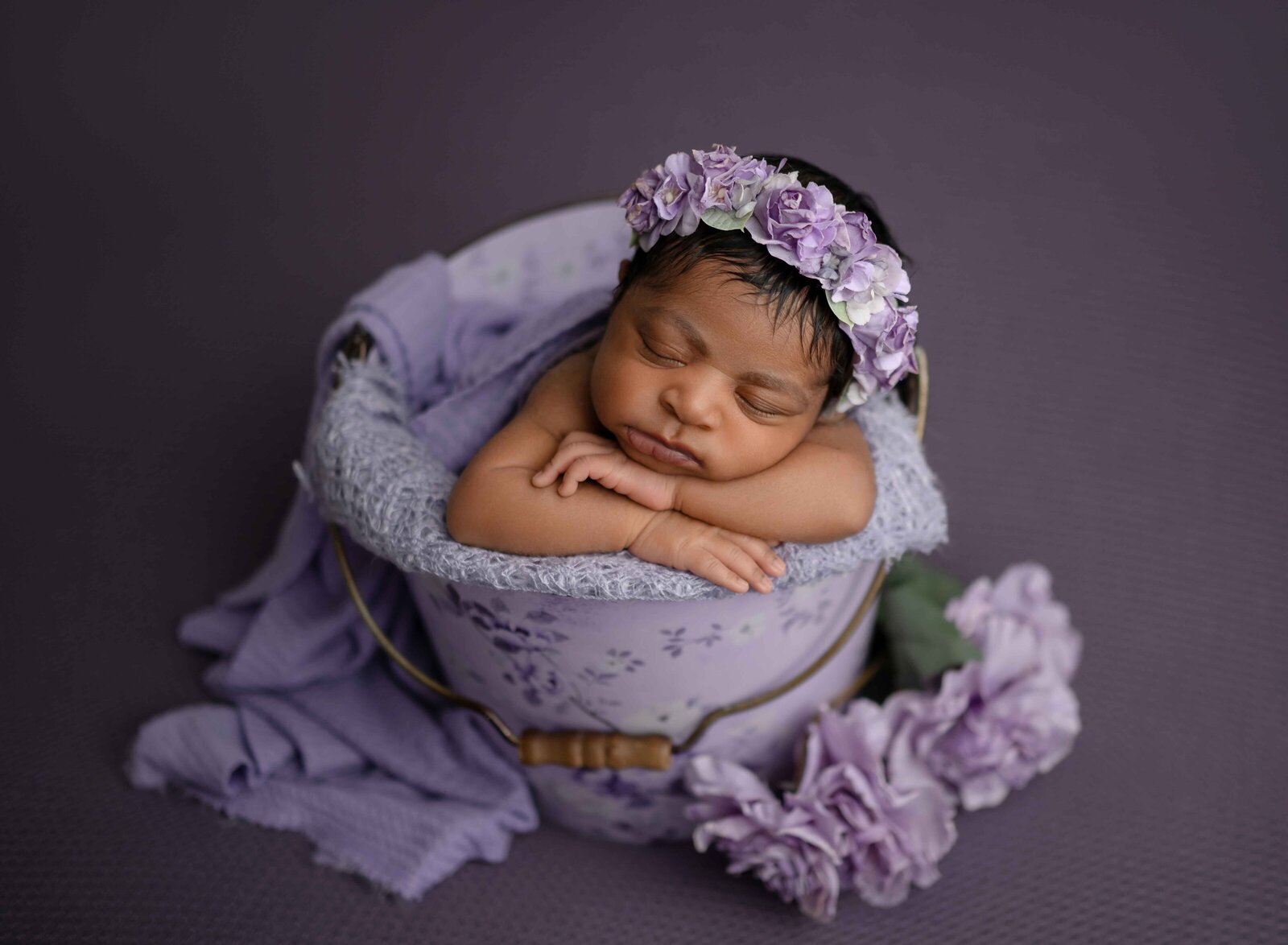 Baby girl sleeping on her hands in a floral purple bucket.