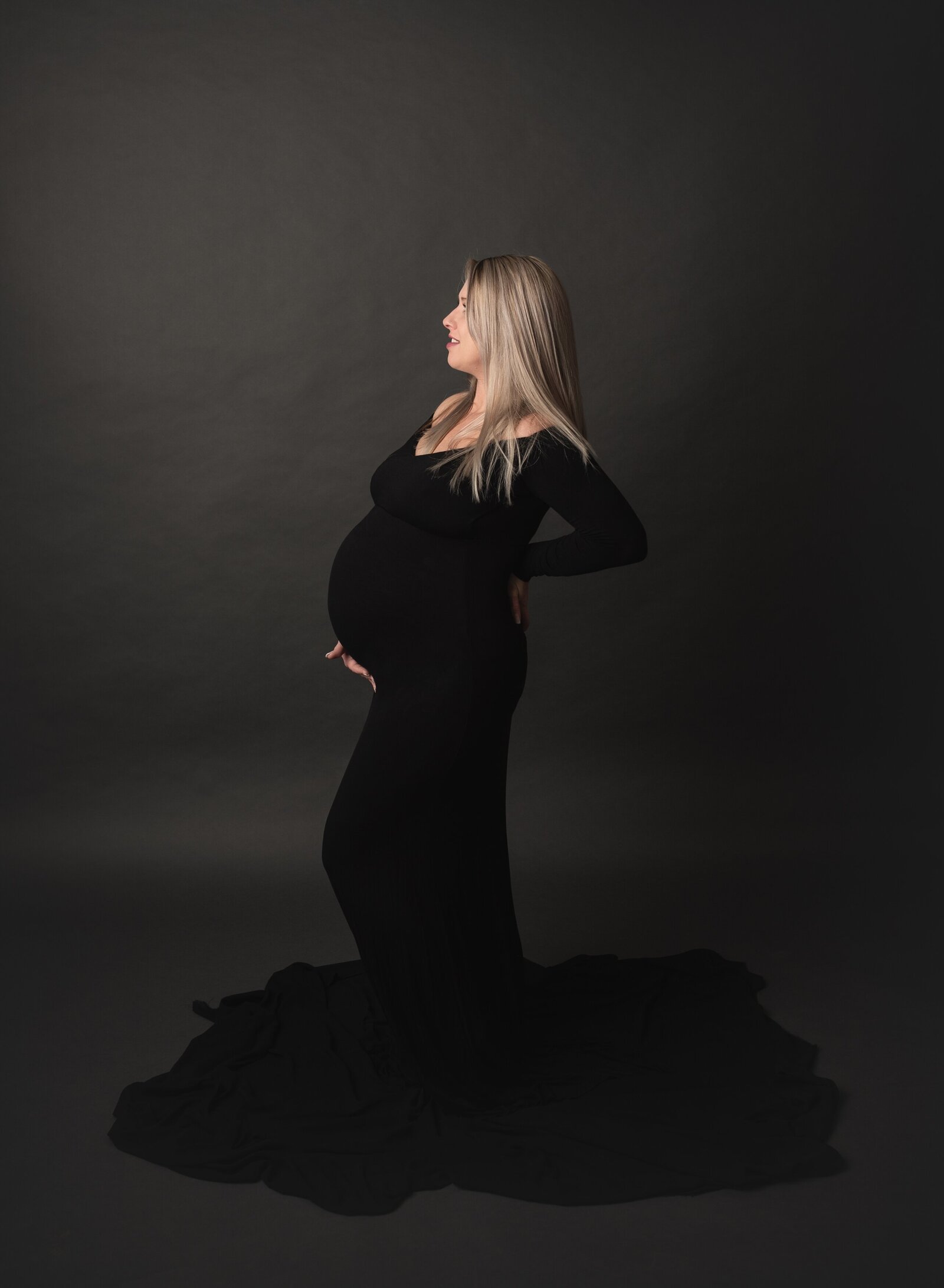 woman wearing a black gown and posing in a studio for her maternity photos