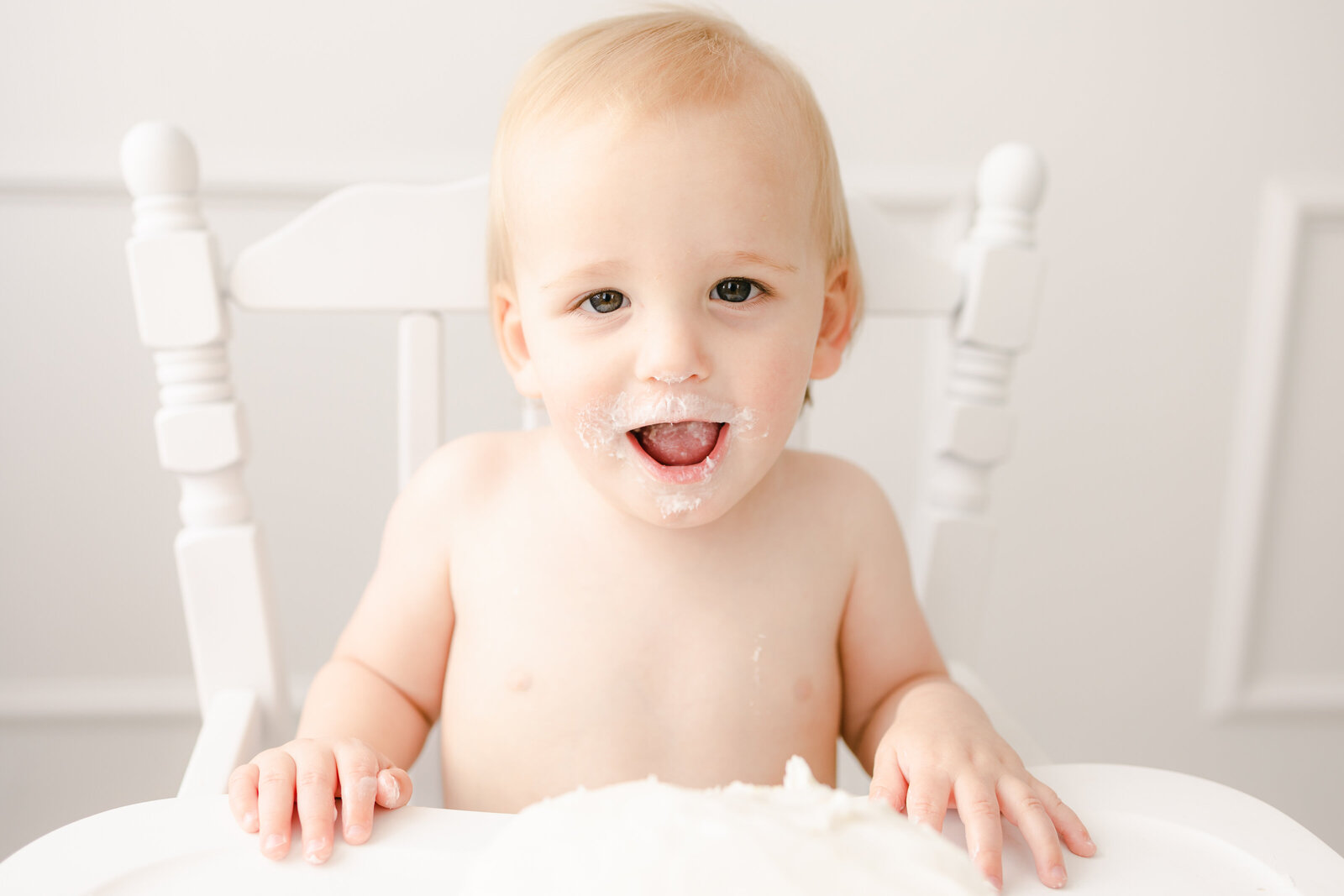 Little boy covered in frosting from his first birthday cake