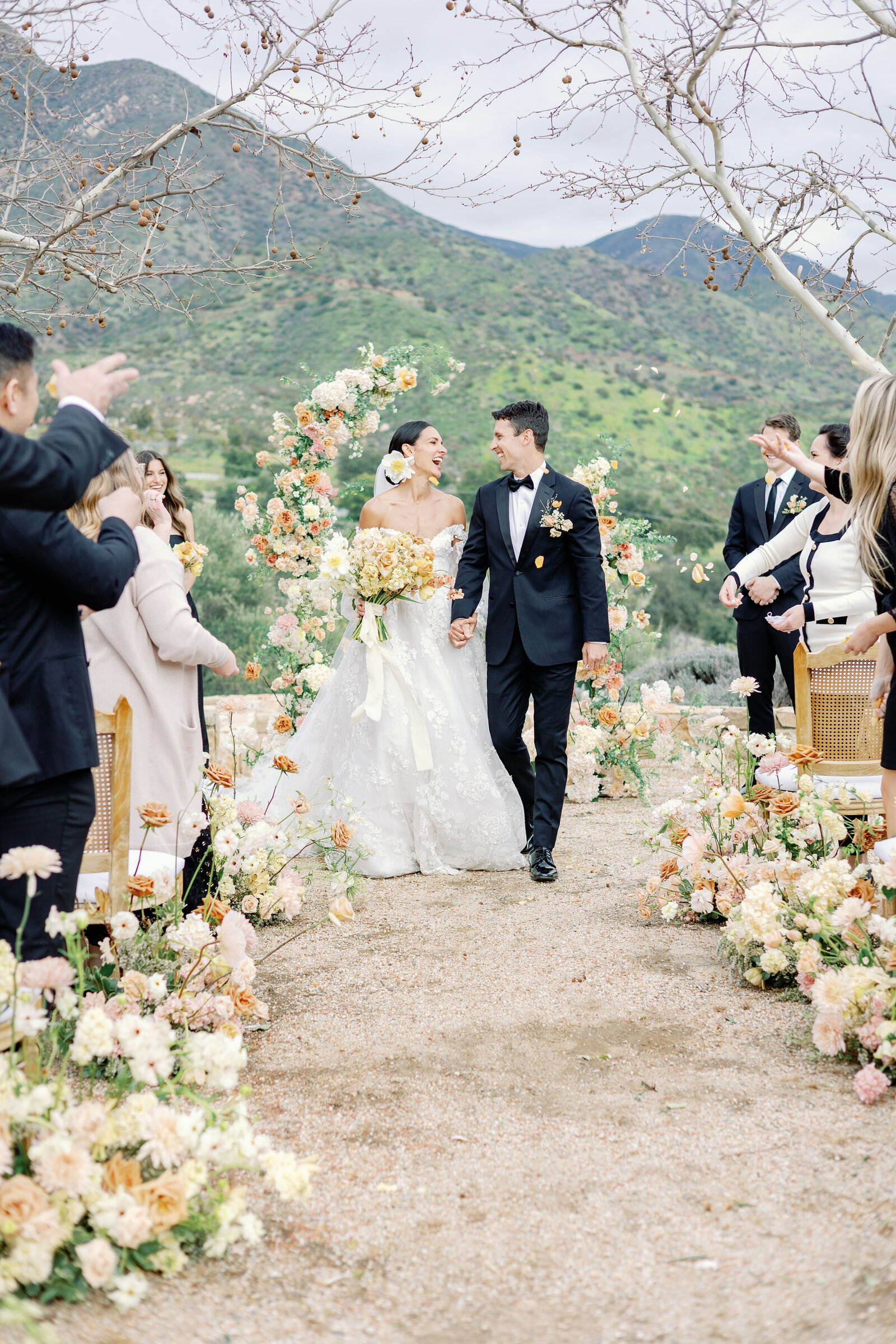 wedding photographer bay area photographs bride adn groom holding hands and exiting their luxury wedding ceremony in Ojai as their guests stand and clap for them