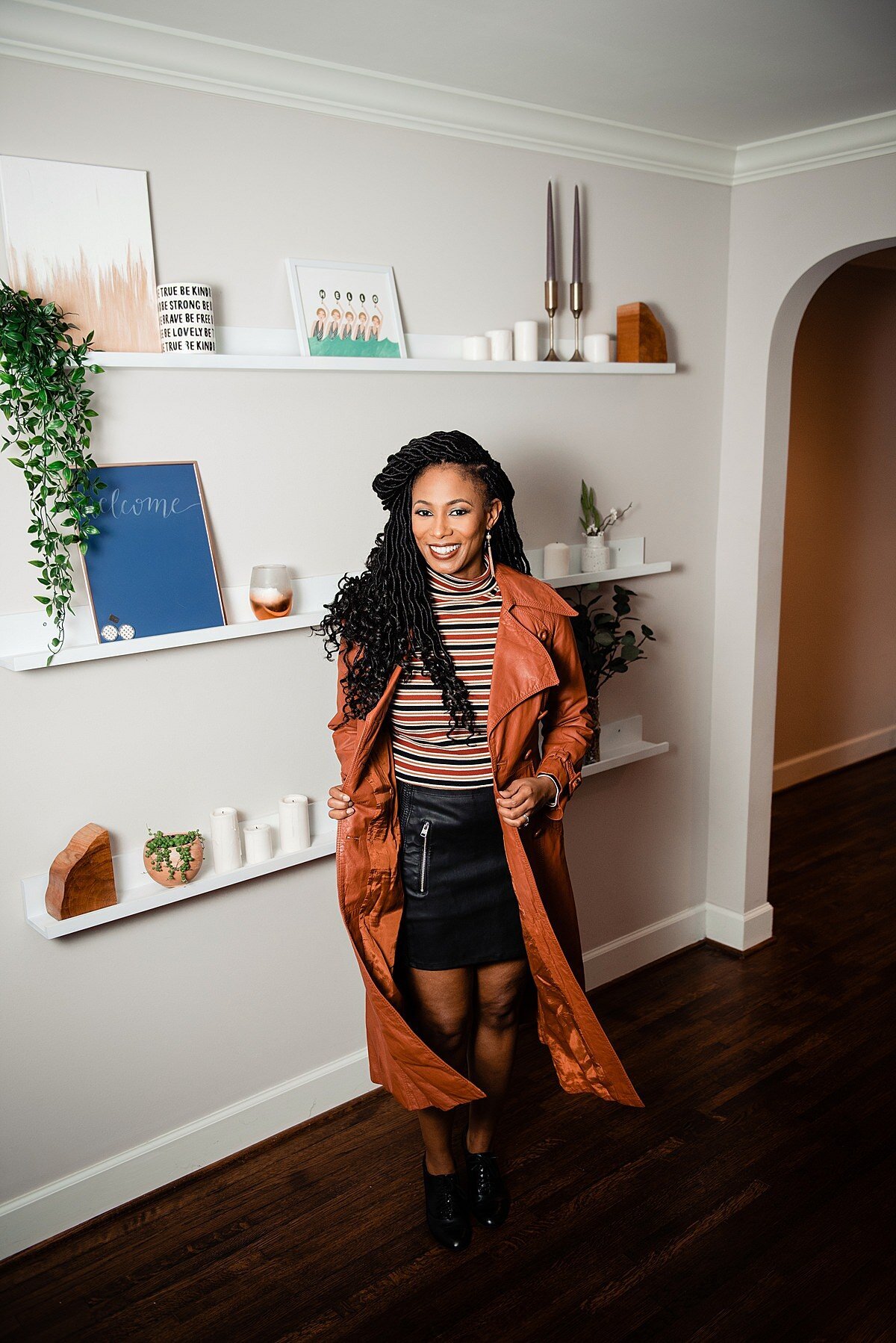 Sheena wearing a black leather skirt, stripped shirt and orange leather trench coast inside kitchen