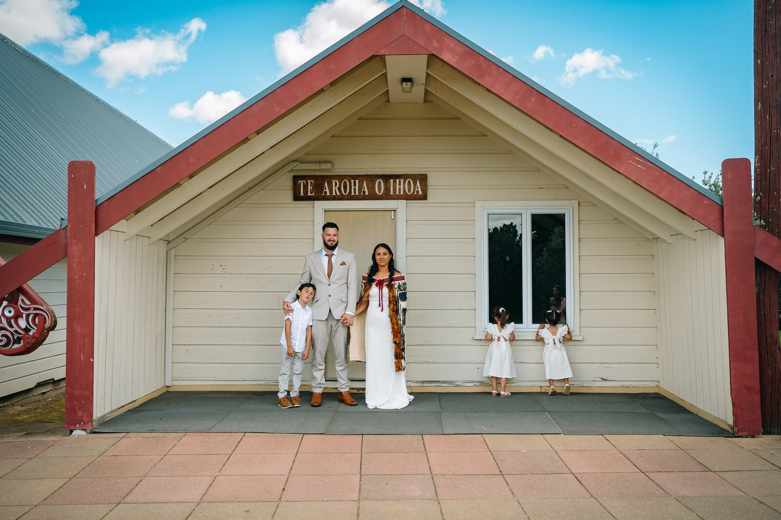 familys wedding photo infront of their Marae, sunny blue skys and little kids 