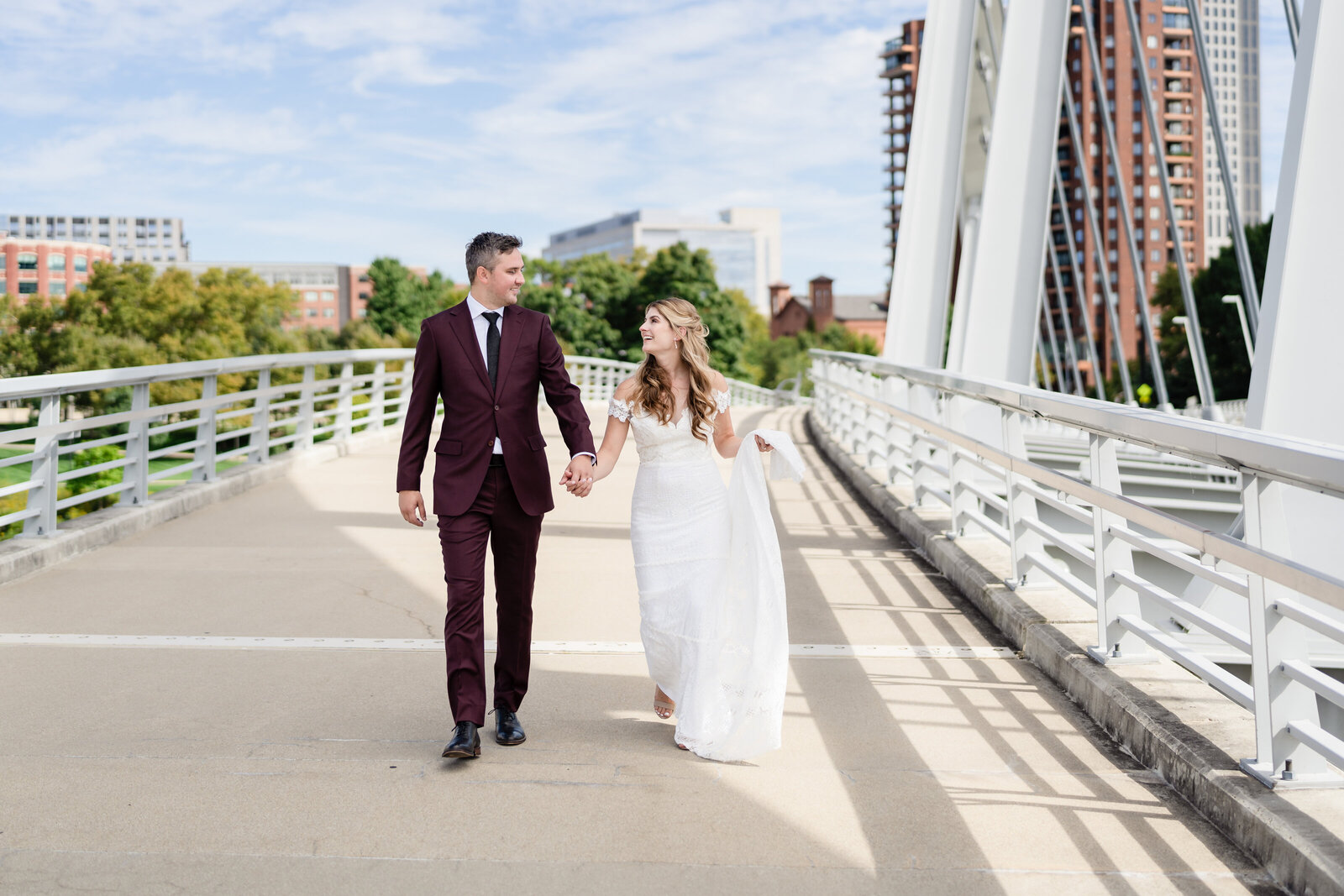 A bride and groom hold hands and walk along the Main Street bridge after their first look