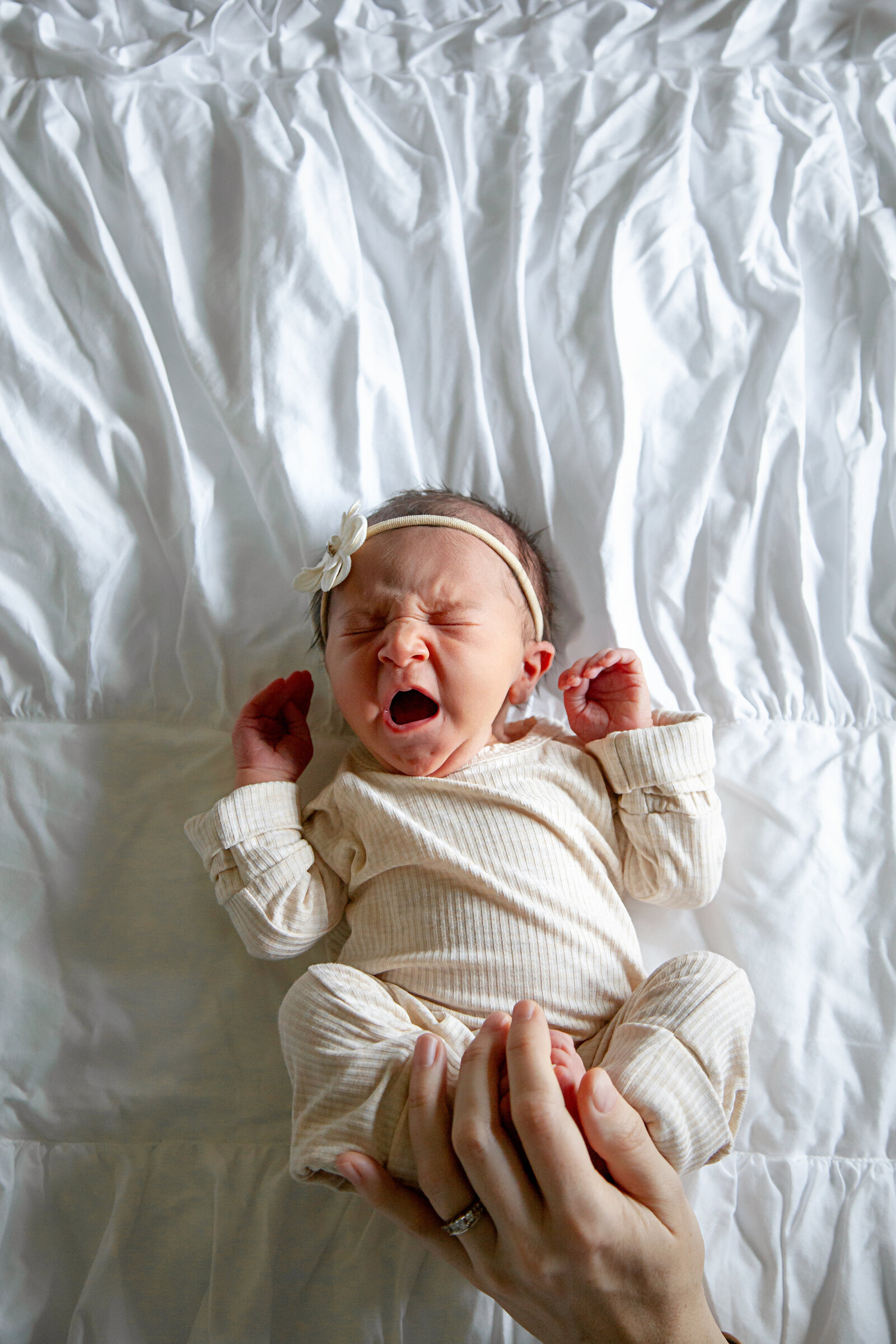 Newborn baby girl lying on white comforter, yawning.