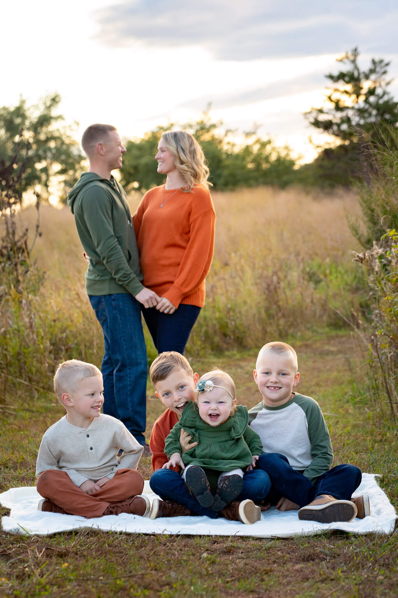 Four siblings sitting on a blanket with their parents standing behind them.