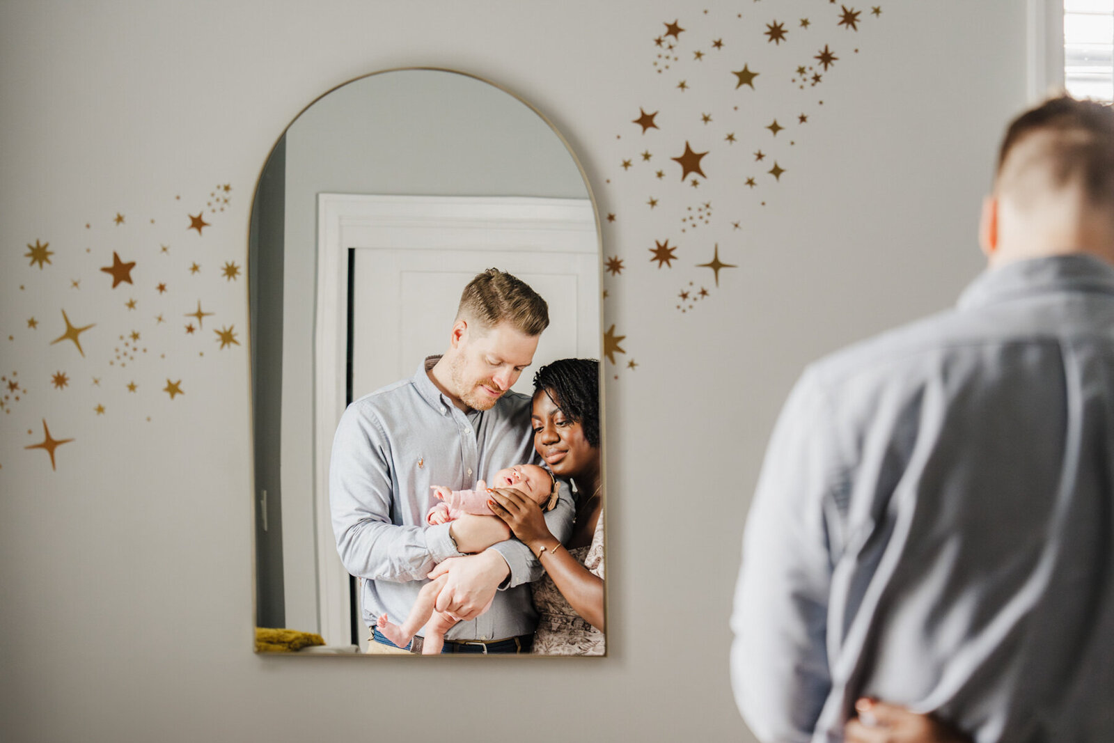 a mirror shows the reflection of parents gazing down at their newborn baby in nursery