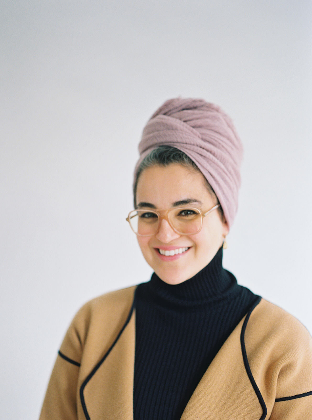 Studio portrait of a smiling woman in a pink headwrap, exuding confidence and charm.