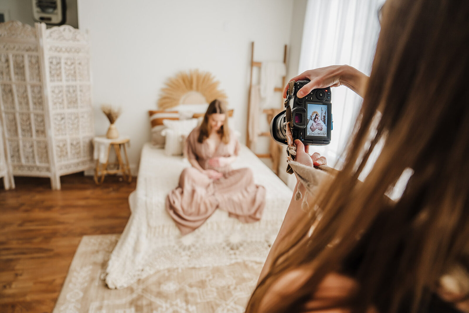 photographer holds up camera to take photo of pregnant woman on bed