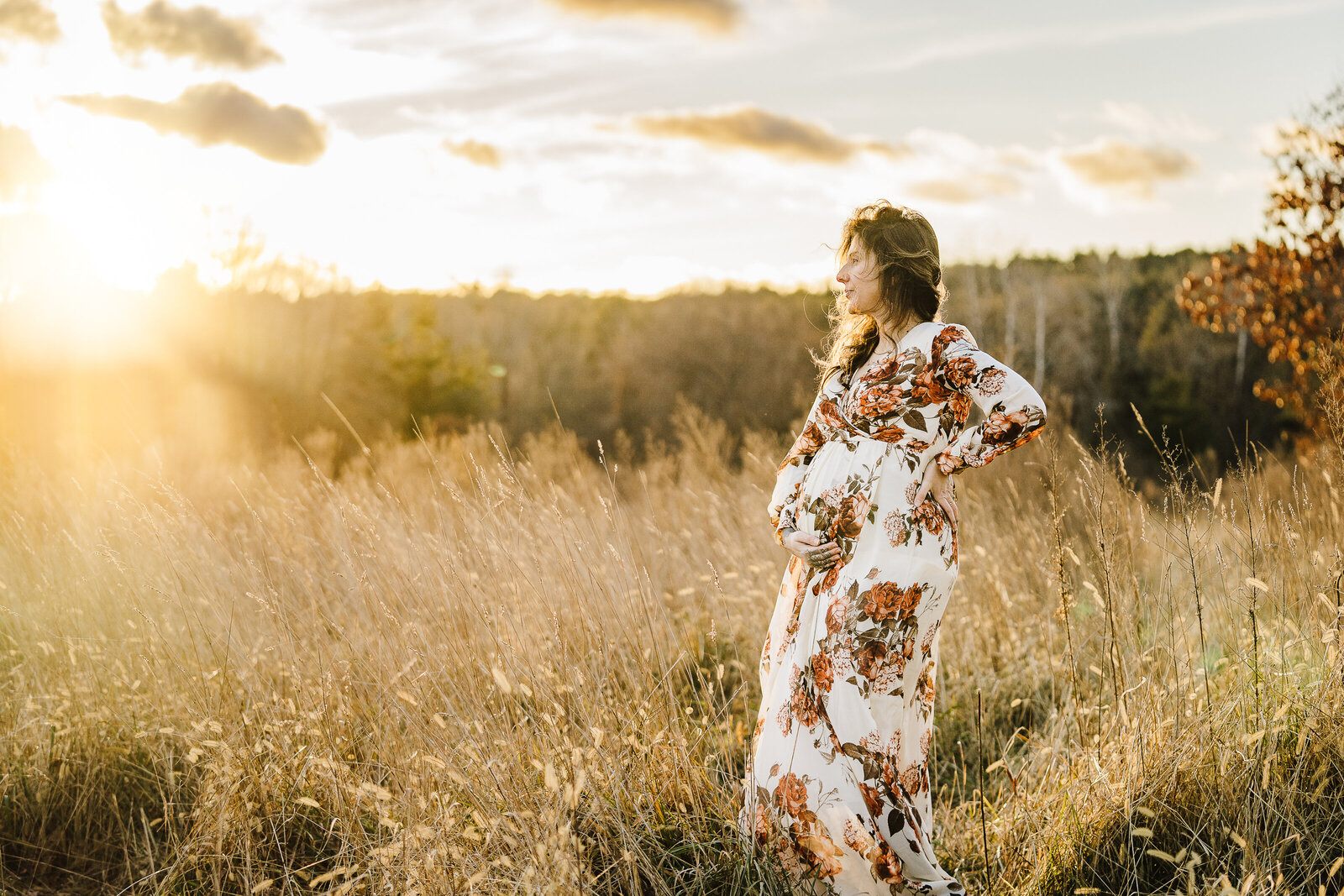 woman holds pregnant belly and stares at sunset