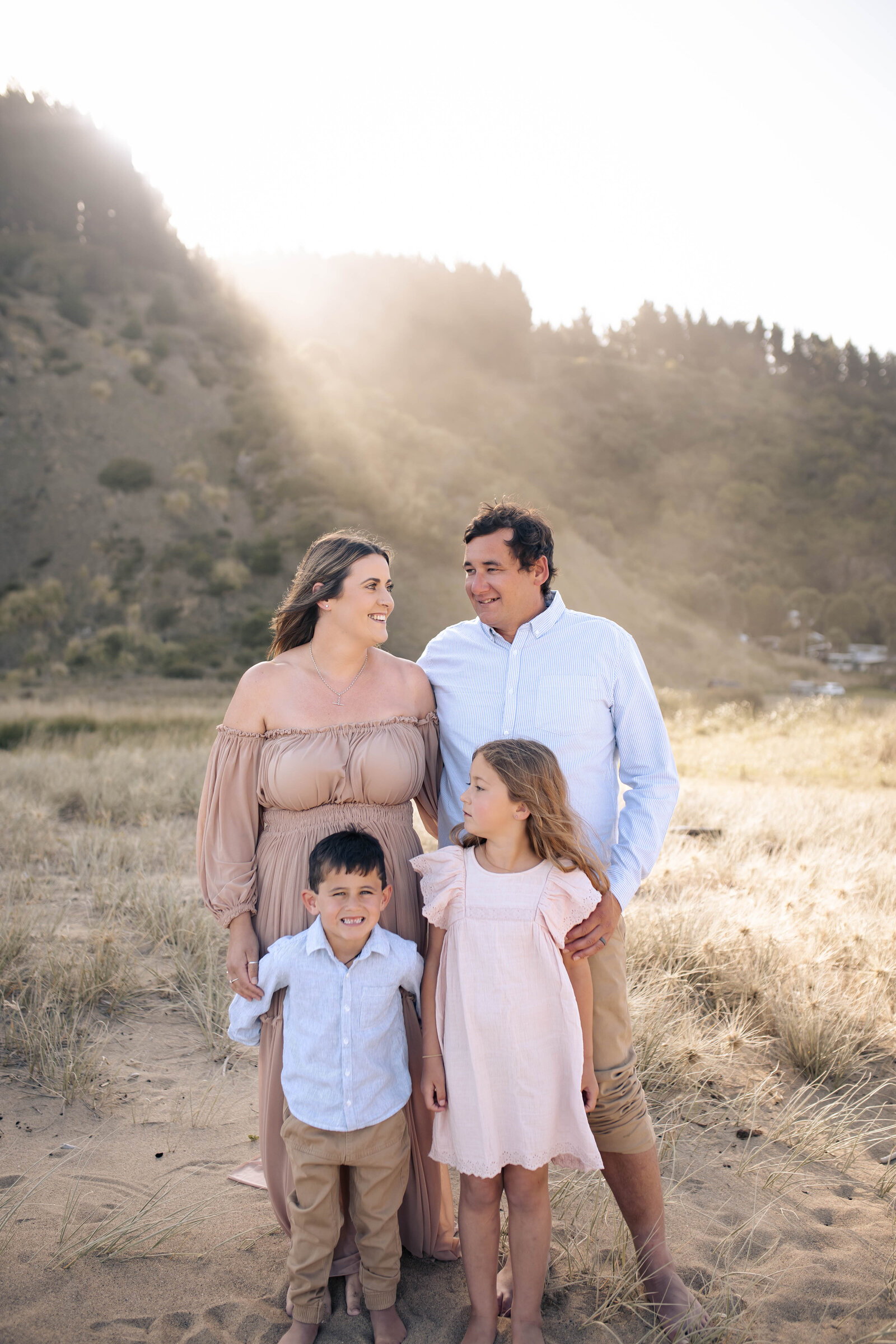 Family cuddling at Waipatiki Beach at sunset, dressed in soft neutral tones from client wardrobe – Hawke’s Bay family photography with natural, emotive style