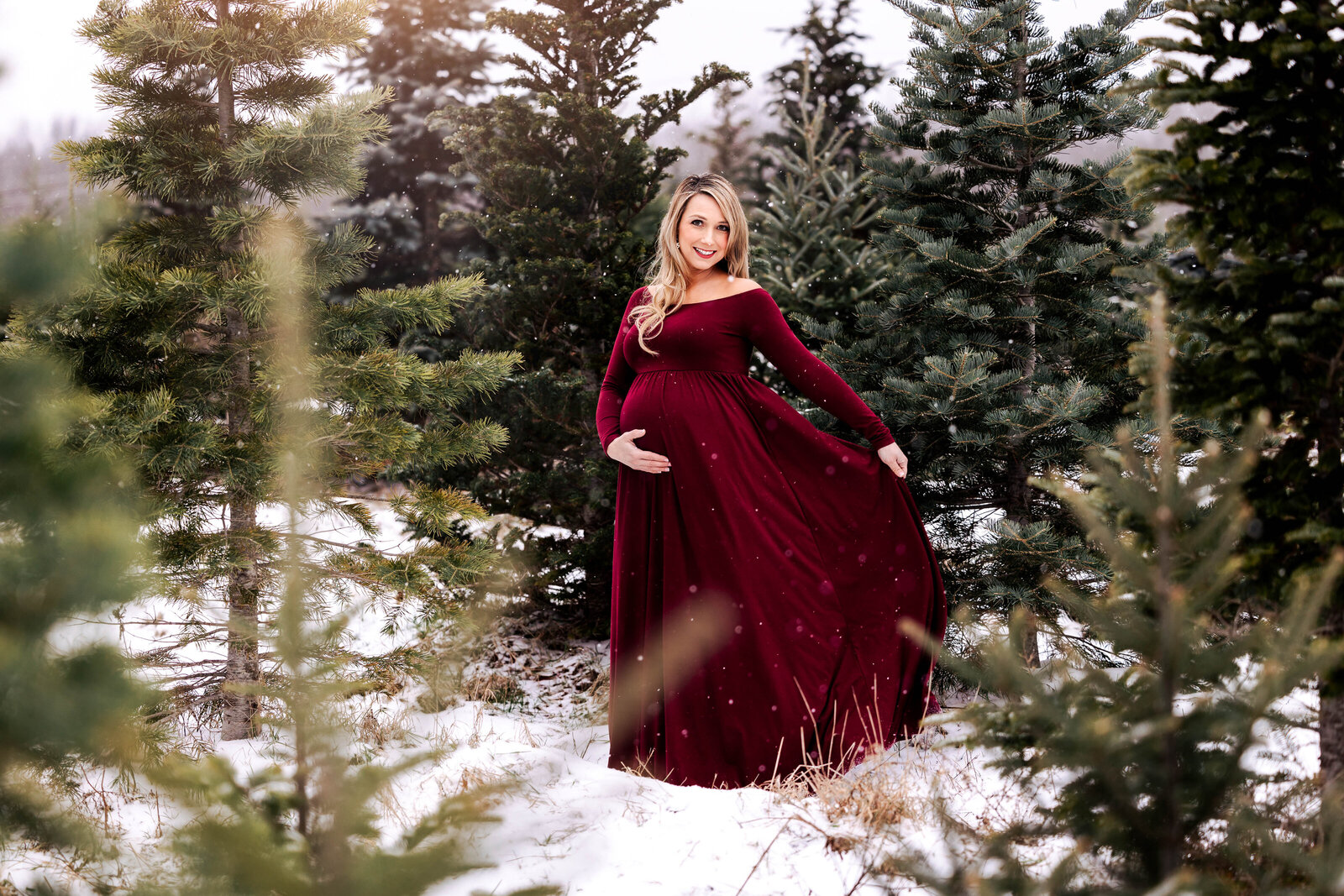 Mother-to-be in red gown poses amongst a field of pine trees
