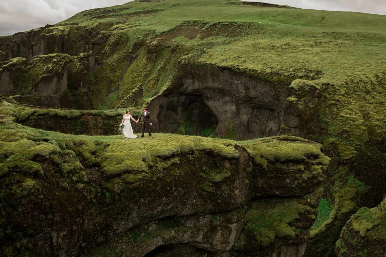A bride and groom walk across a lush grassy hillside on their Iceland elopement. 