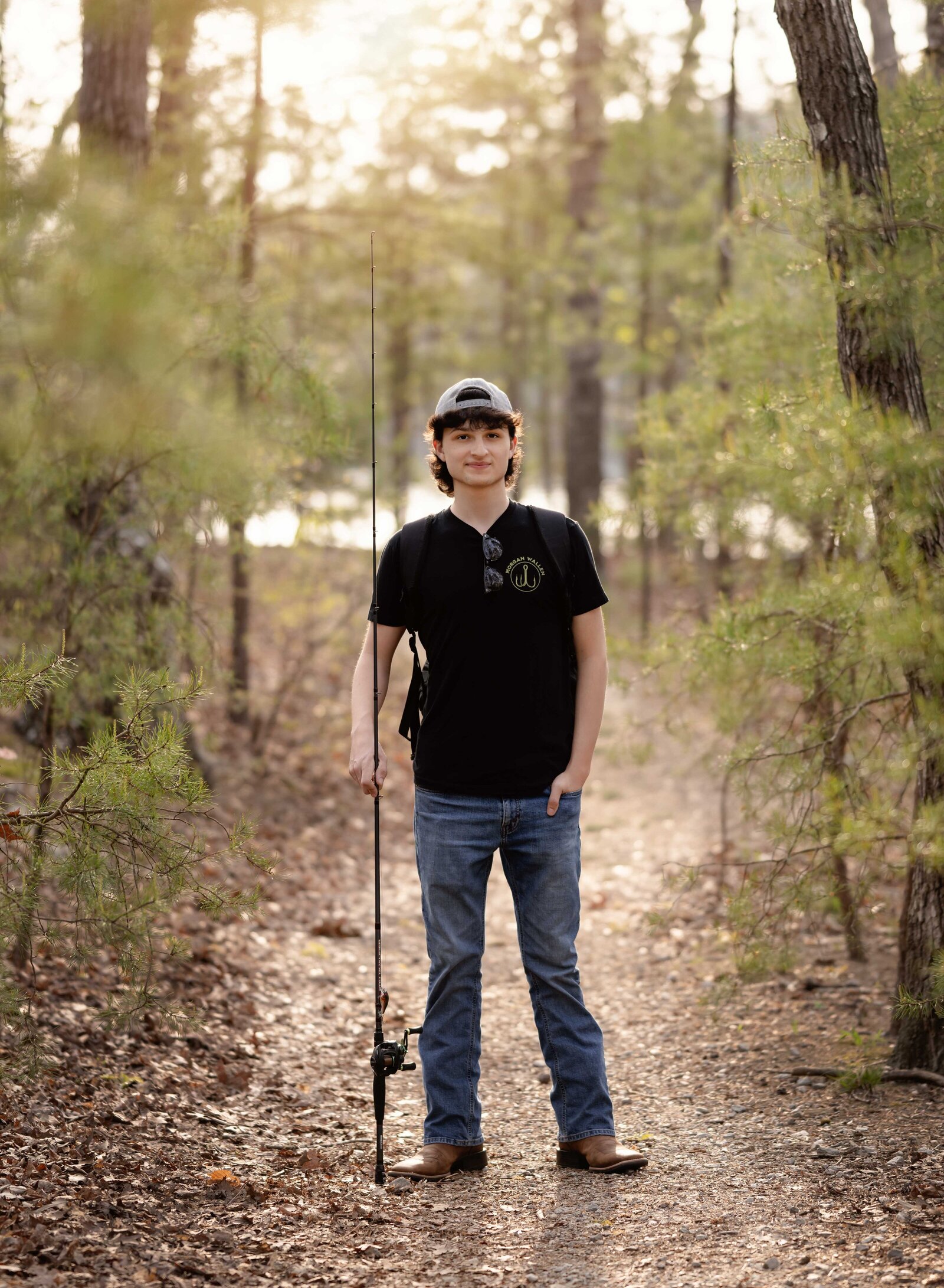 Senior photo of boy in woods holding fishing pole and smiling at the camera. Senior graduation photos taken by Jenni Nikki Photography in Atlanta, GA
