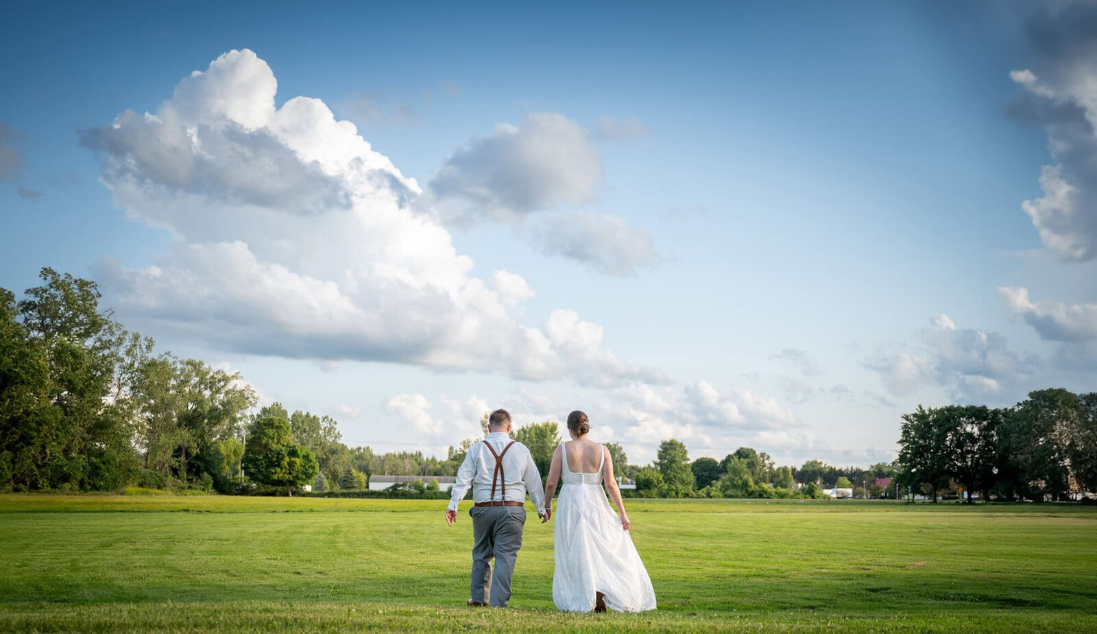 bride and groom walking into field below blue skies