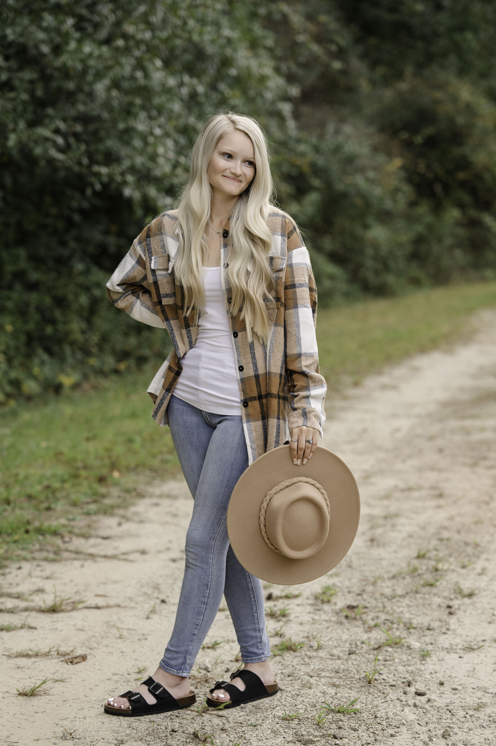 High school senior holds brown hat down by her side and smiles off to the left