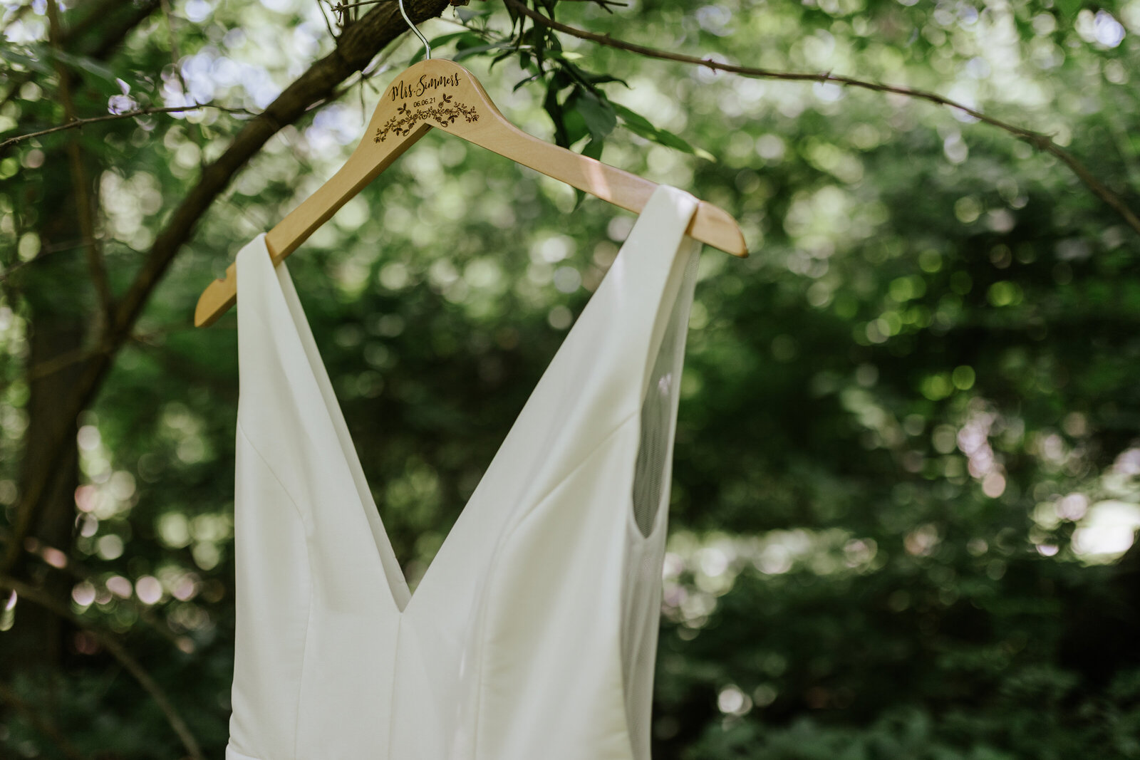 A wedding dress hangs from a tree in the woods on a wooden hanger