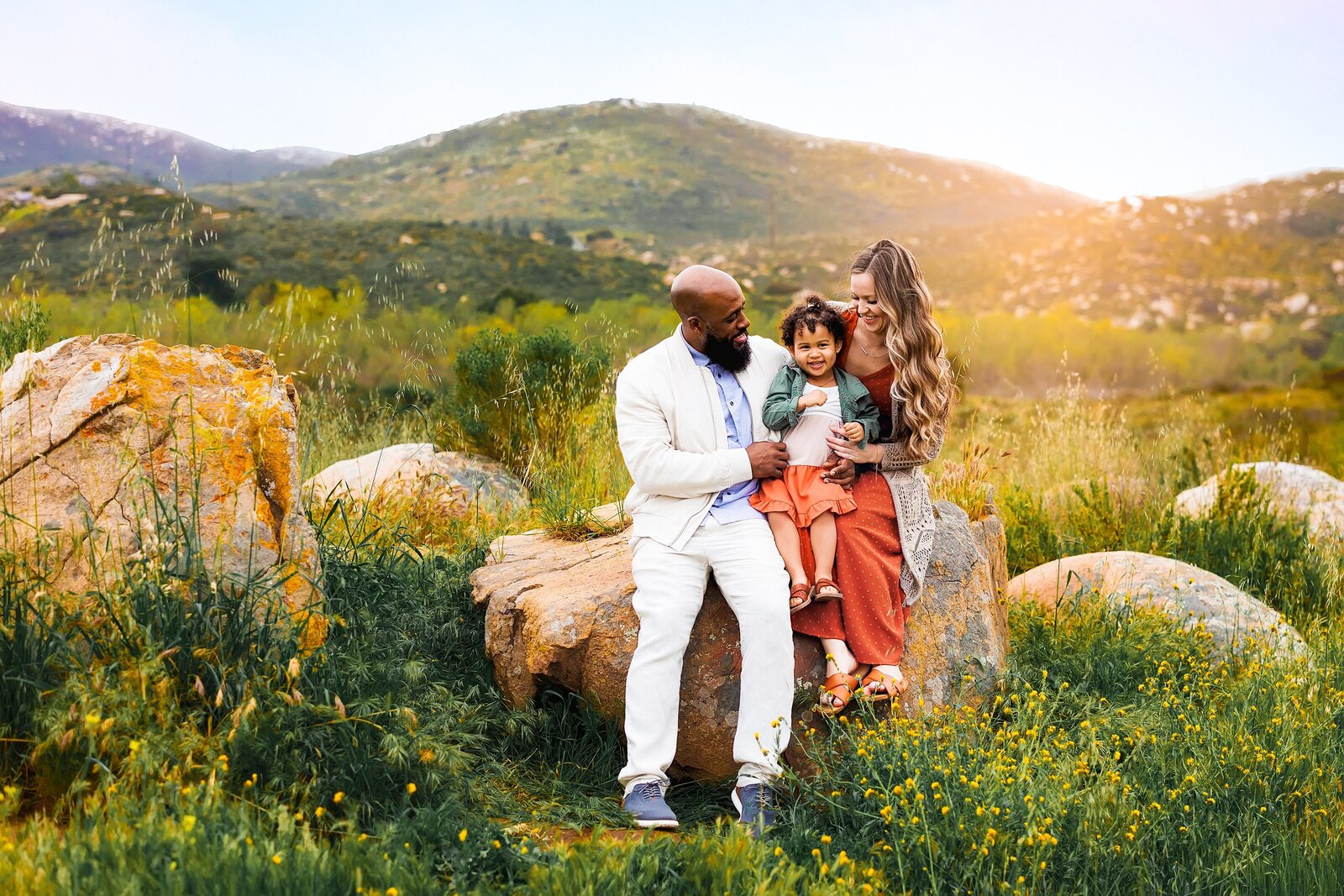 Parents posing with their young daughter, sitting on a rock with mountain views in Rancho Bernardo