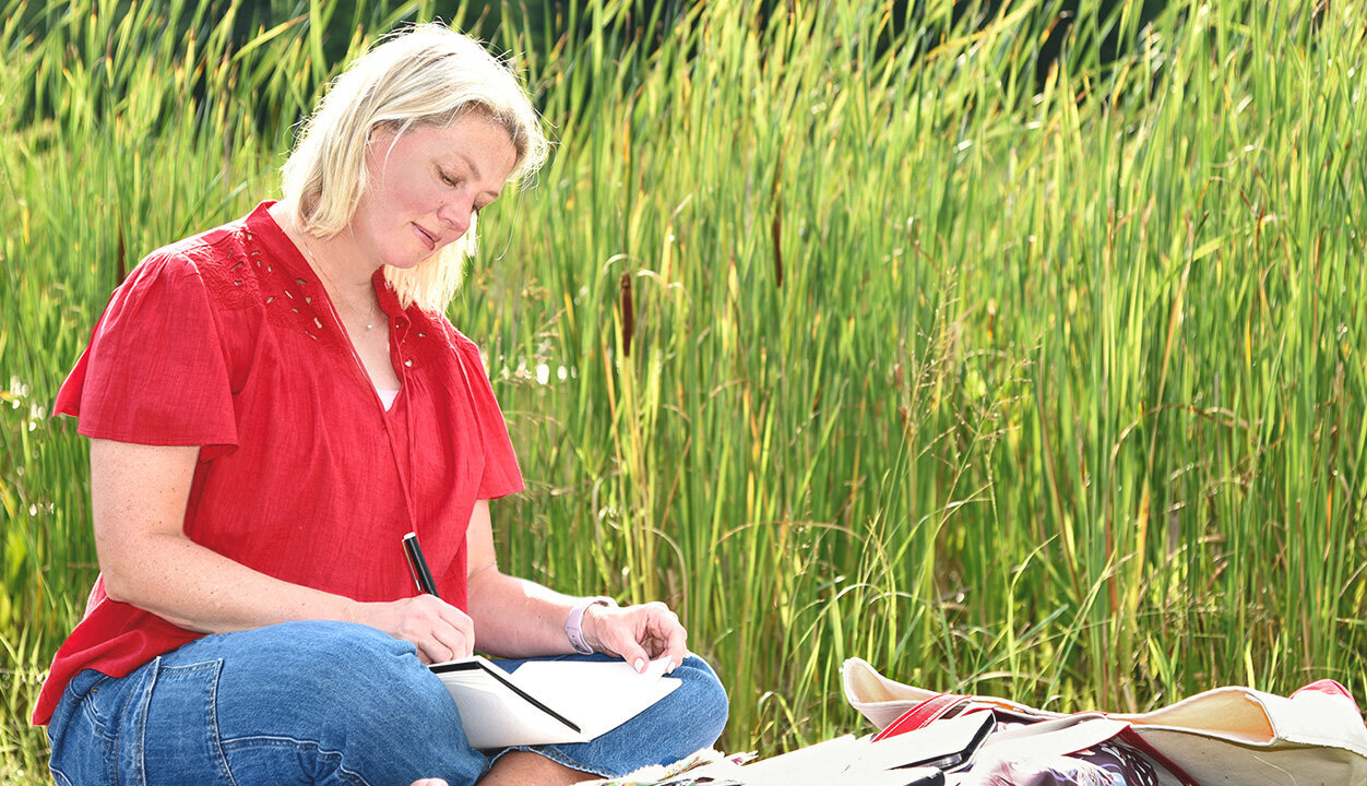 Photo of Ellen Morse sitting outside in nature with sketchbook