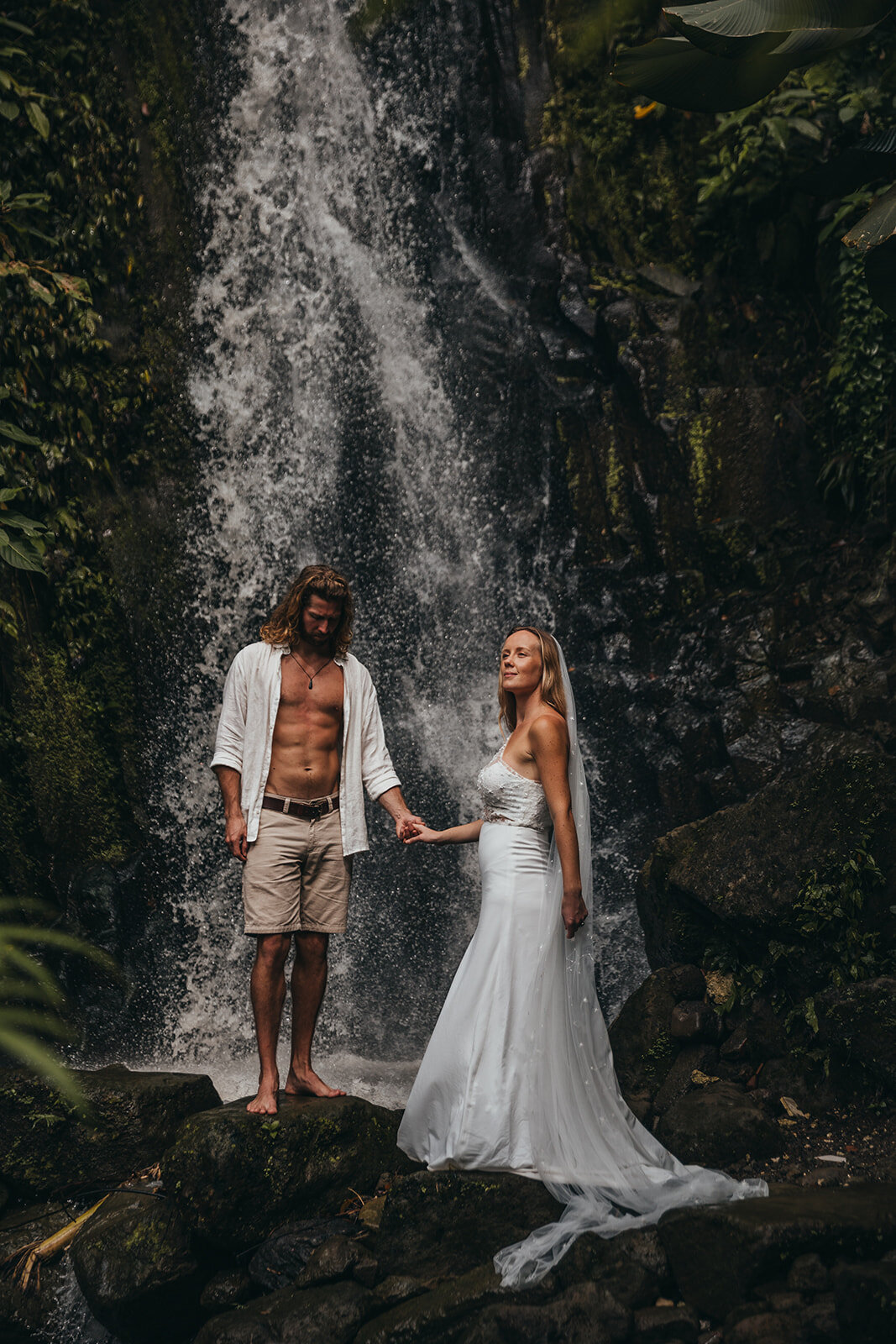 newly-wed couple pose by waterfall