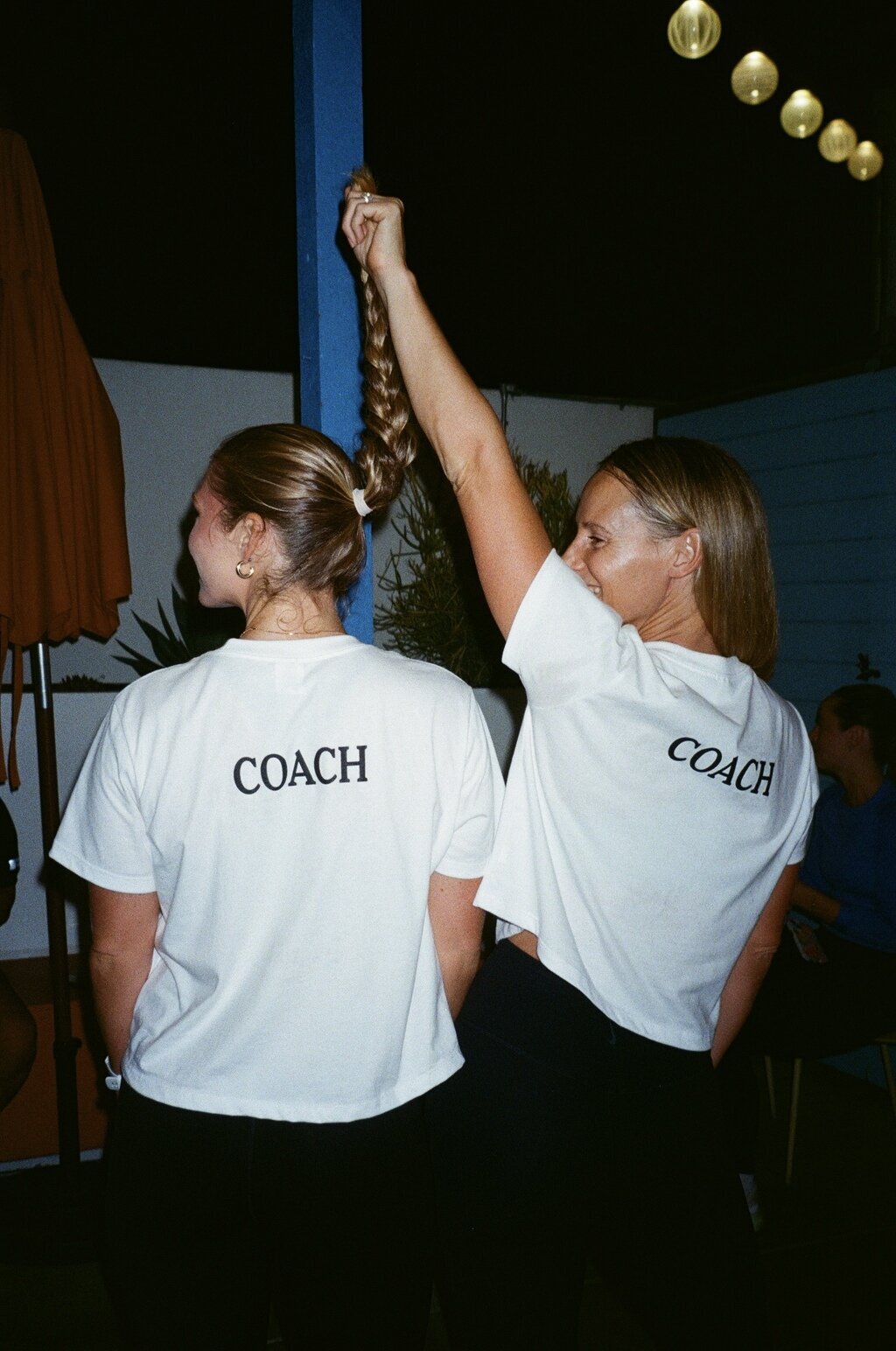 HER Sports Club coaches wearing matching COACH shirts and smiling together.