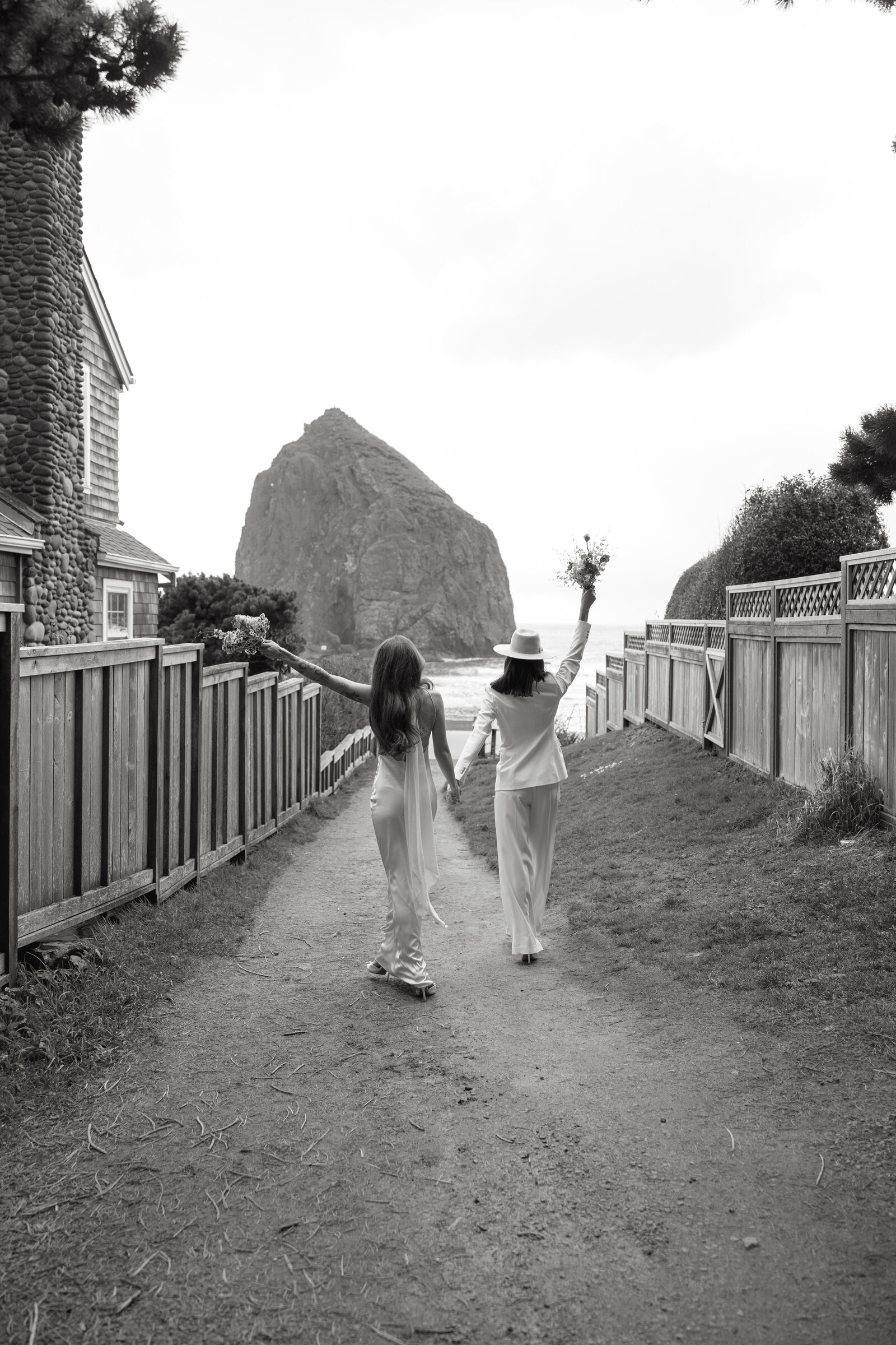 Two brides hold hands as they walk towards a beach after getting married in Vancouver.
