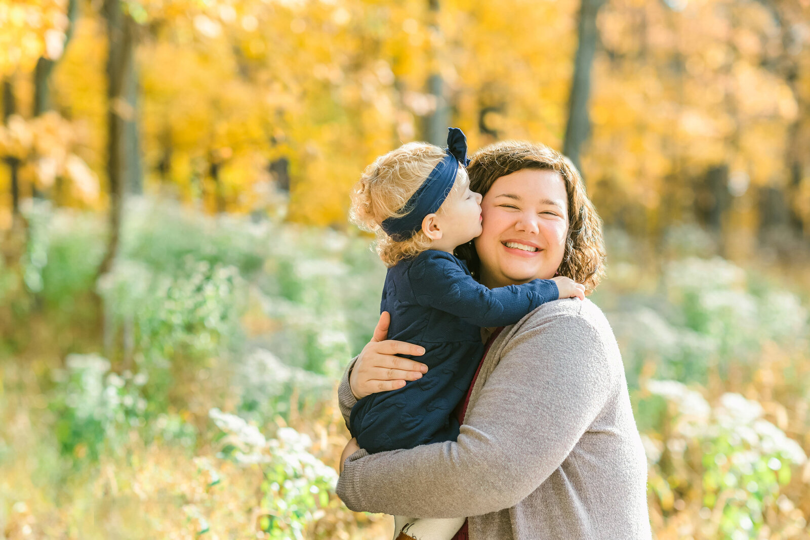 Toddler daughter giving her mom a kiss in the fall woods of Illinois for their Chicago family photos.