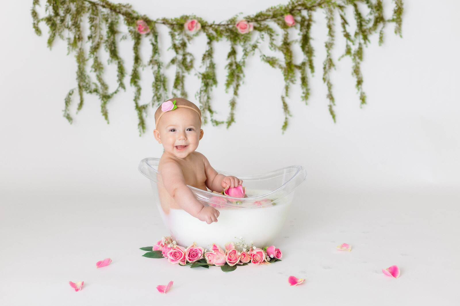 Milestone Photographer, a baby girl sits in a glass tub of milk and roses, she smiles