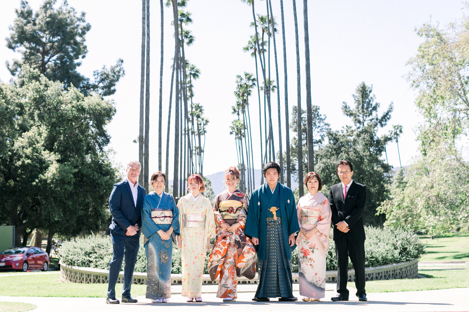 Extended family group photo lined with tall palm trees at Brand Park for a Seijinshiki (coming-of-age) celebration—furisode and hakama kimono rental in Los Angeles | ブランドパークのヤシ並木を背景に成人式を祝う家族集合写真。振袖と袴の着物レンタル。