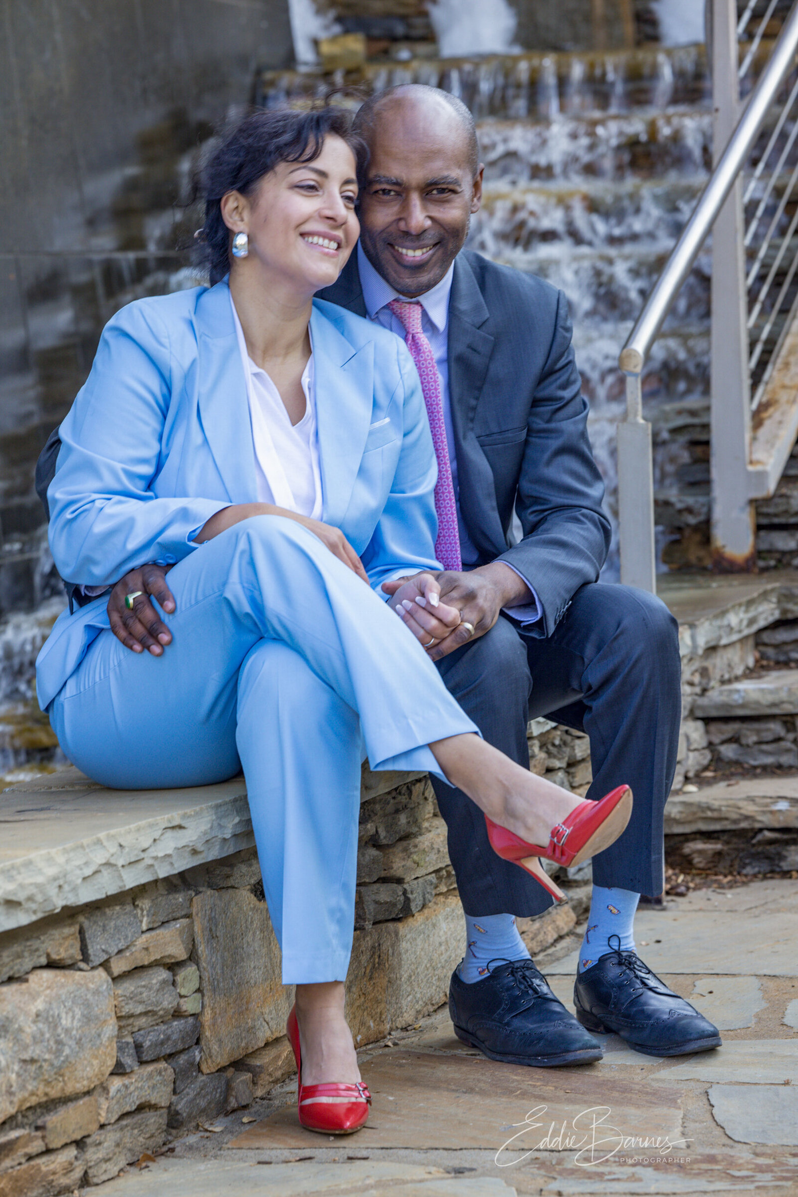Outdoor portrait of a smiling couple sitting by a waterfall, photographed by Tytanium3 Photography, a professional photographer in Simpsonville, SC.