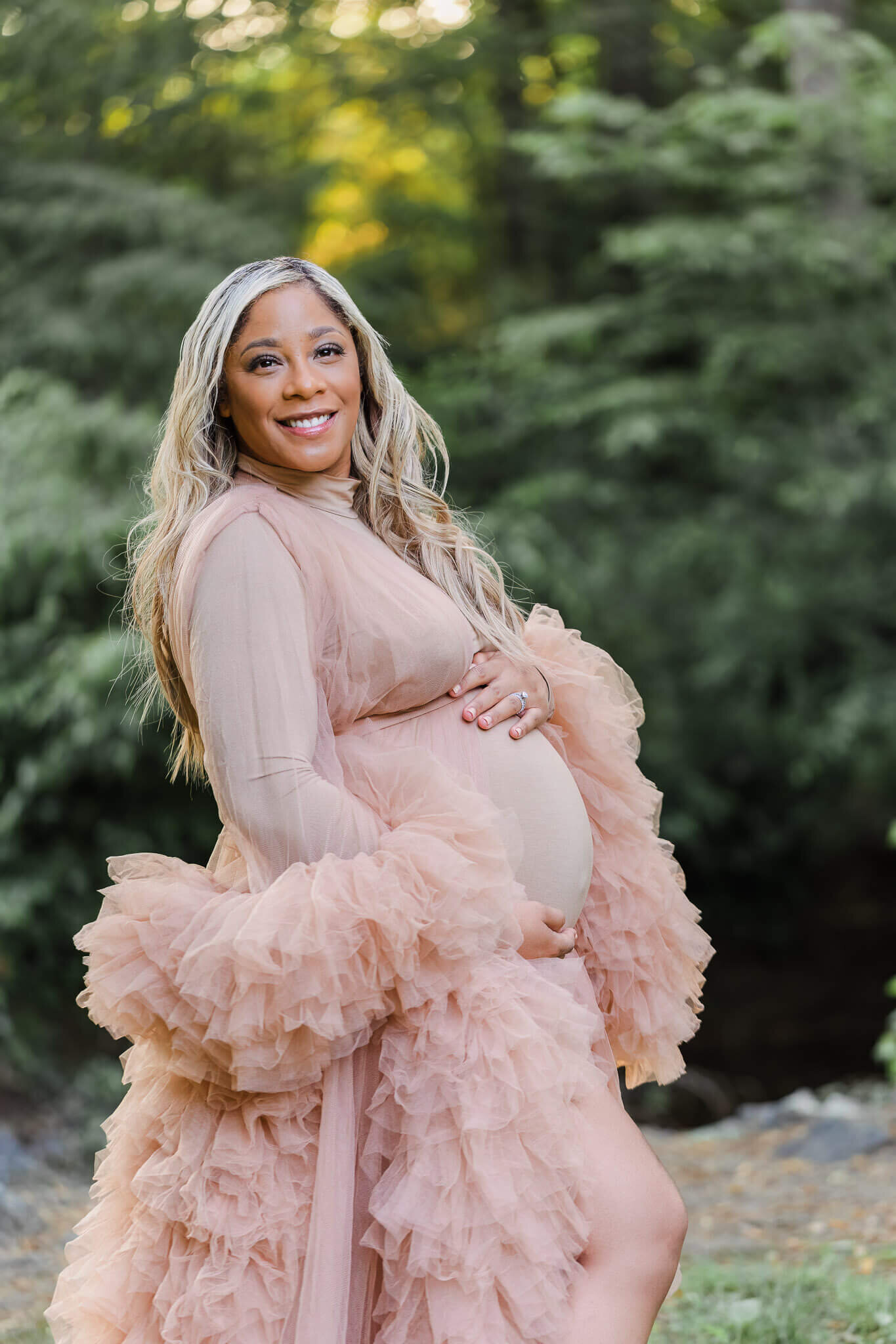 A pregnant woman in a tan robe hugging her belly.