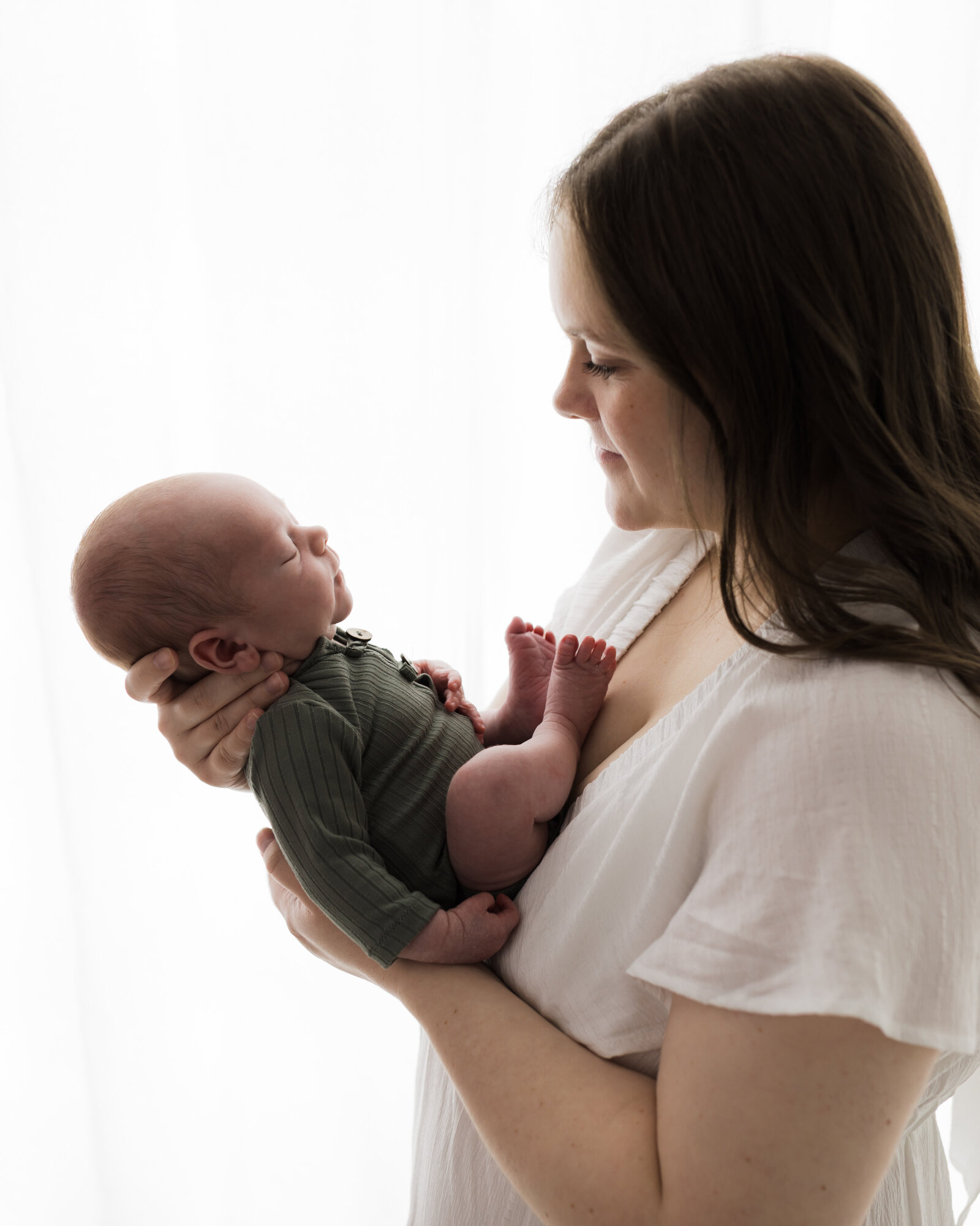 mom in white dress holding newborn baby boy in green swaddle for studio portraits cleveland newborn photographer
