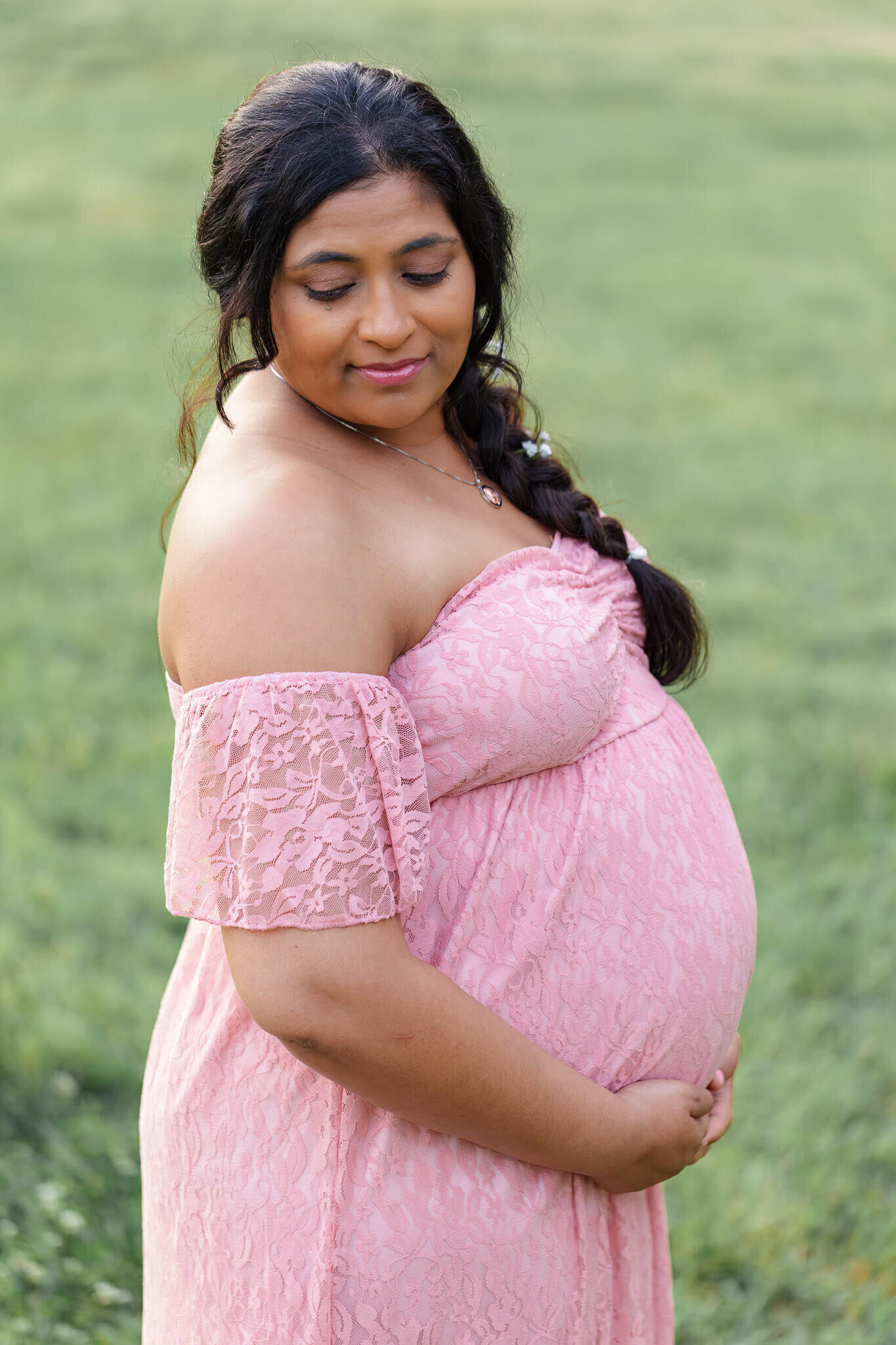 A mother-to-be wearing a pink dress and posing in a grassy field in Alexandria, VA.
