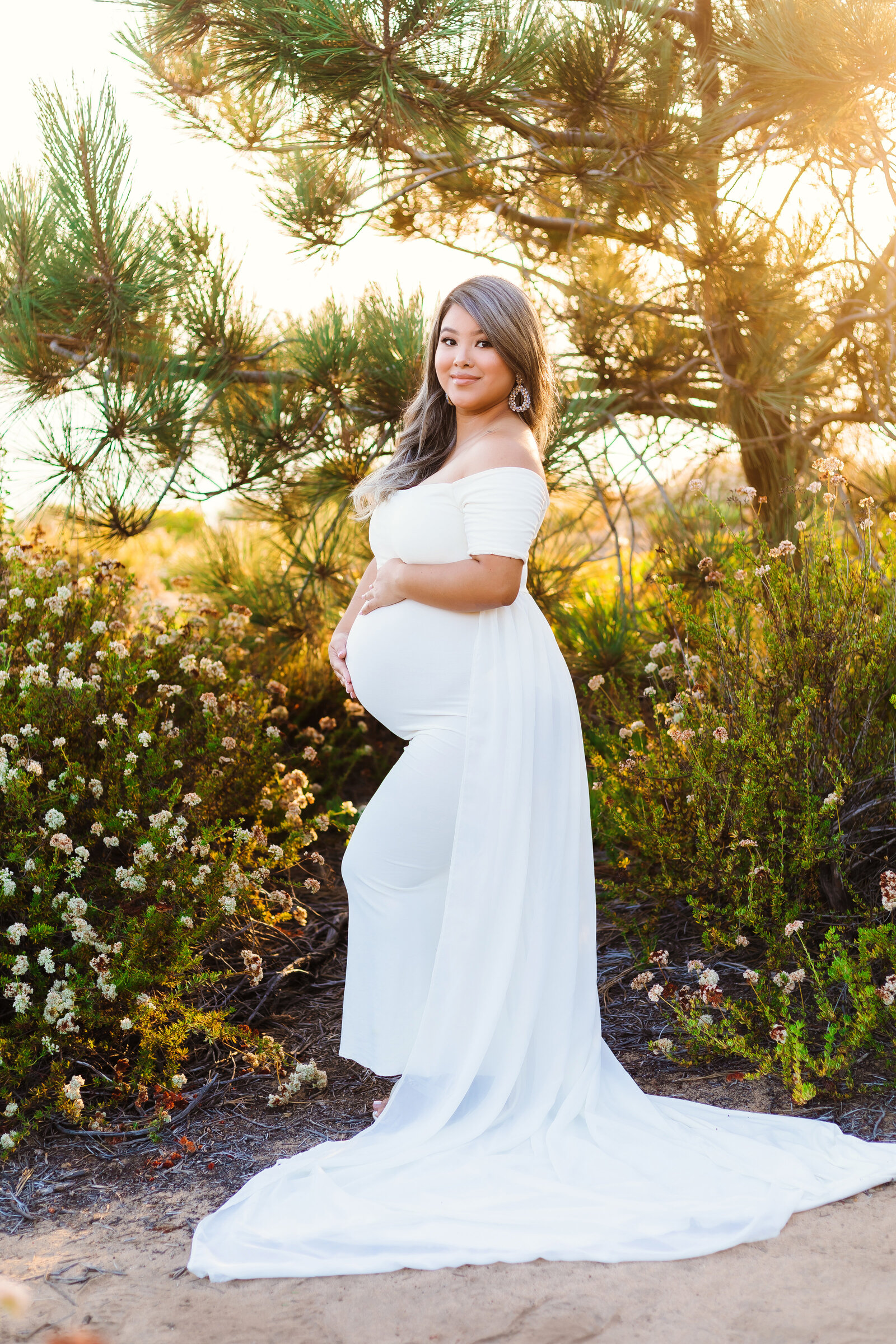 Maternity Photographer, a pregnant woman stands happy with hands on her belly near chaparral