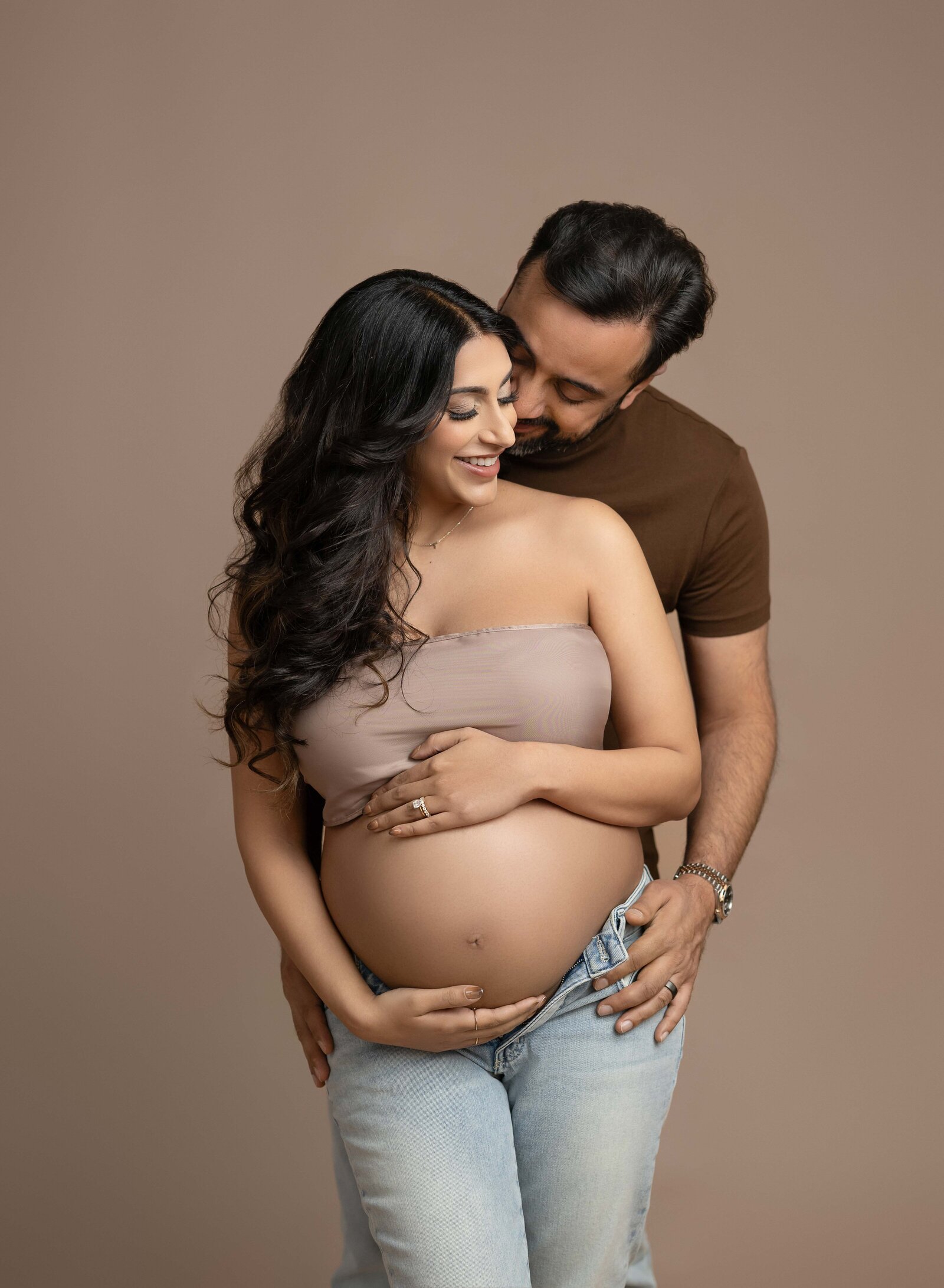 Mom and Dad snuggling and Dad whispering in Mom's ear while holding baby bump. Photo taken at Atlanta Maternity photo studio in Woodstock, GA.